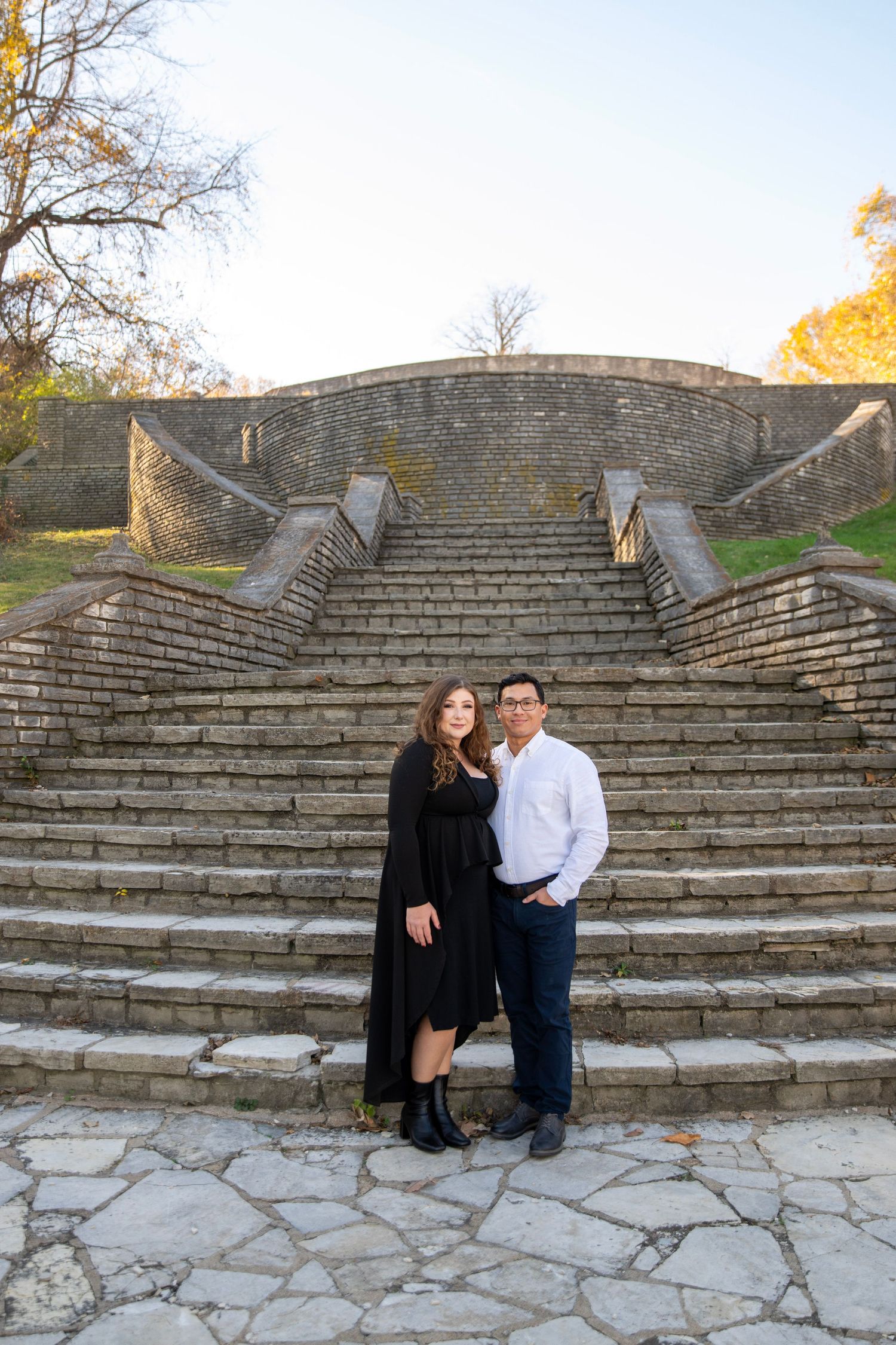 A couple sits together on historic stone steps surrounded by autumn foliage.