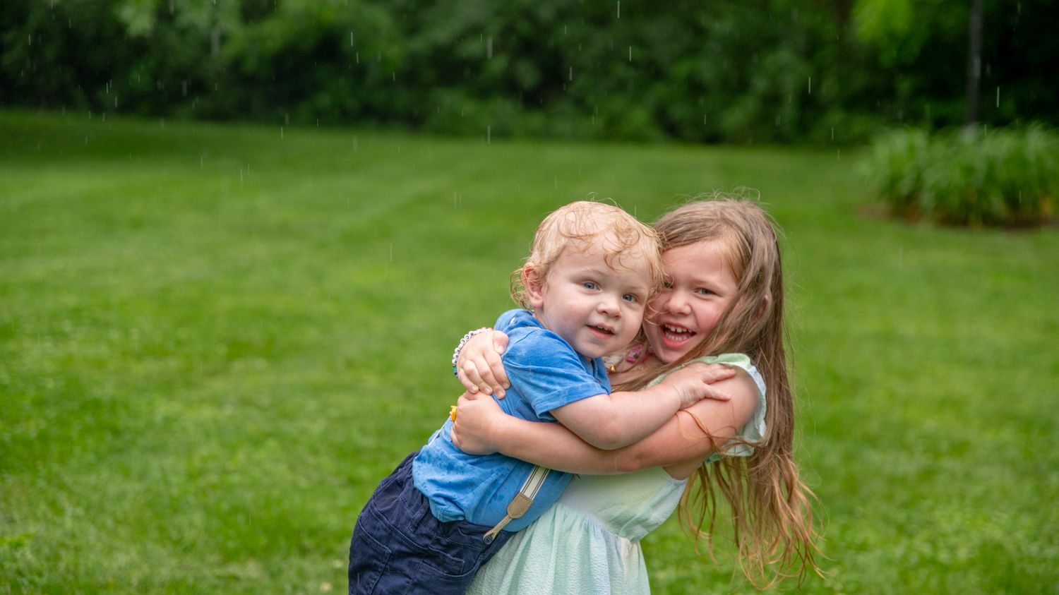 Two children embrace while playing on a green lawn on a summer day.