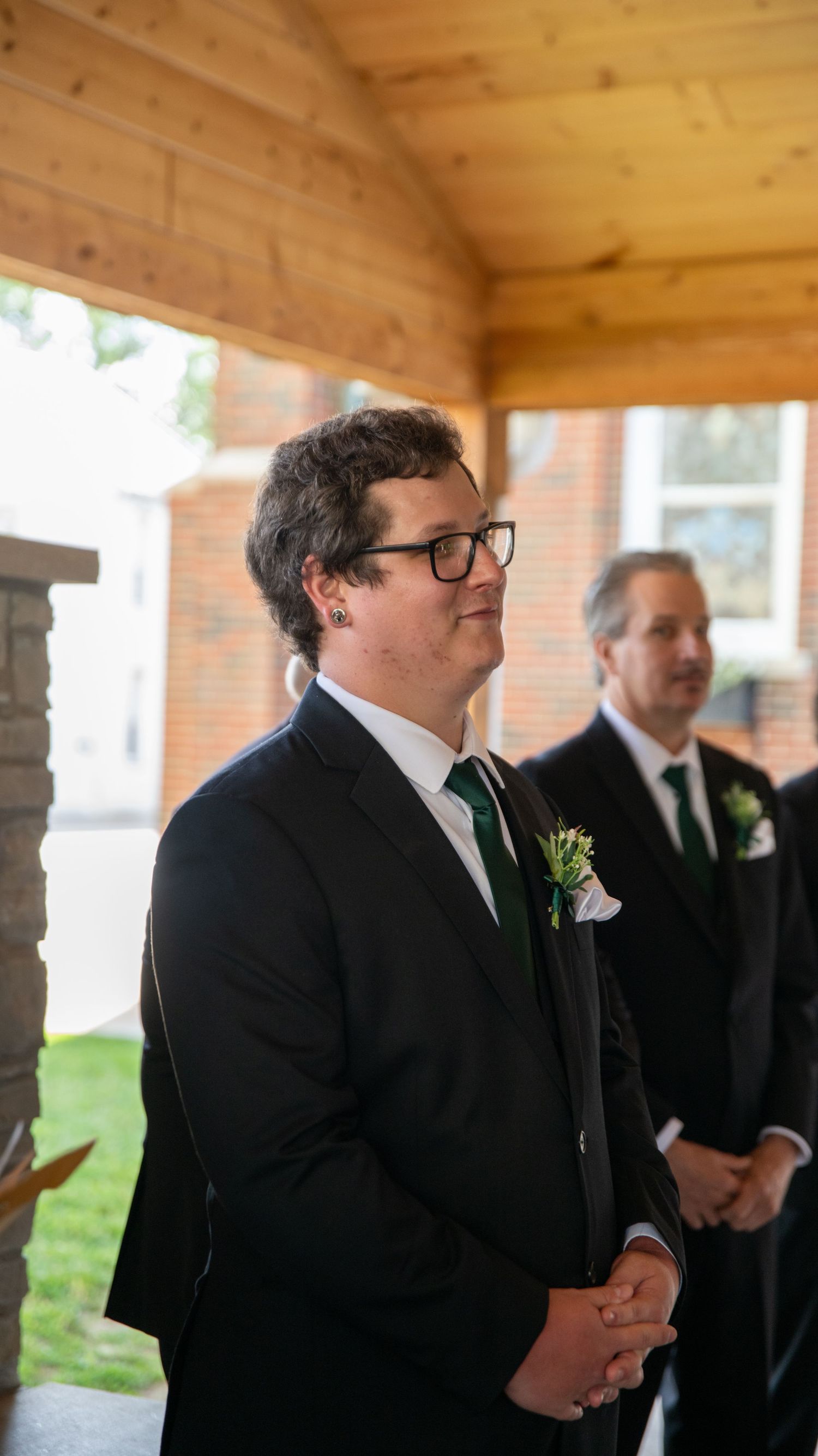 Groomsmen in black suits and green ties waiting during a wedding ceremony.