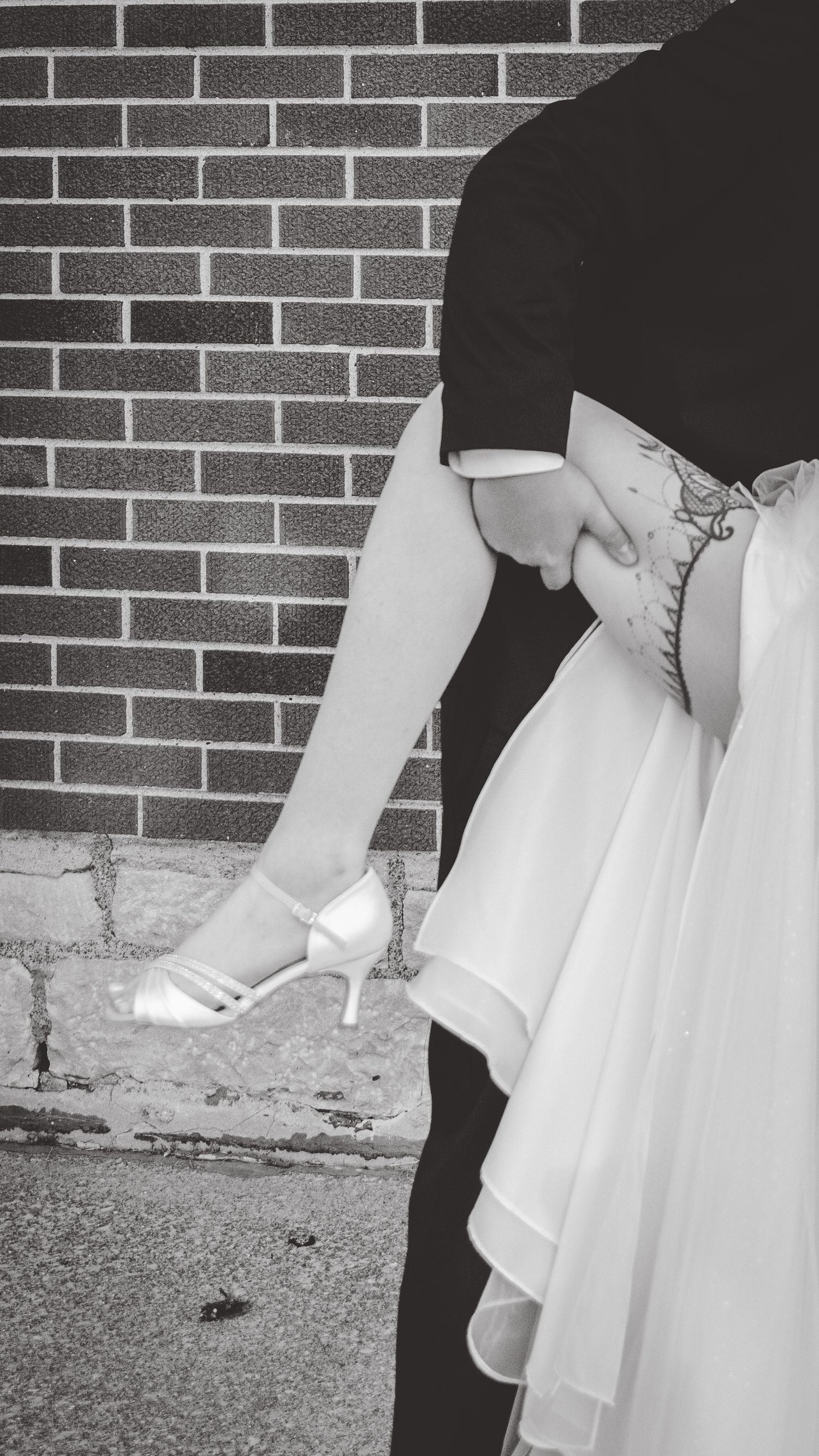 Black and white detail shots of wedding dress and shoes against brick wall.