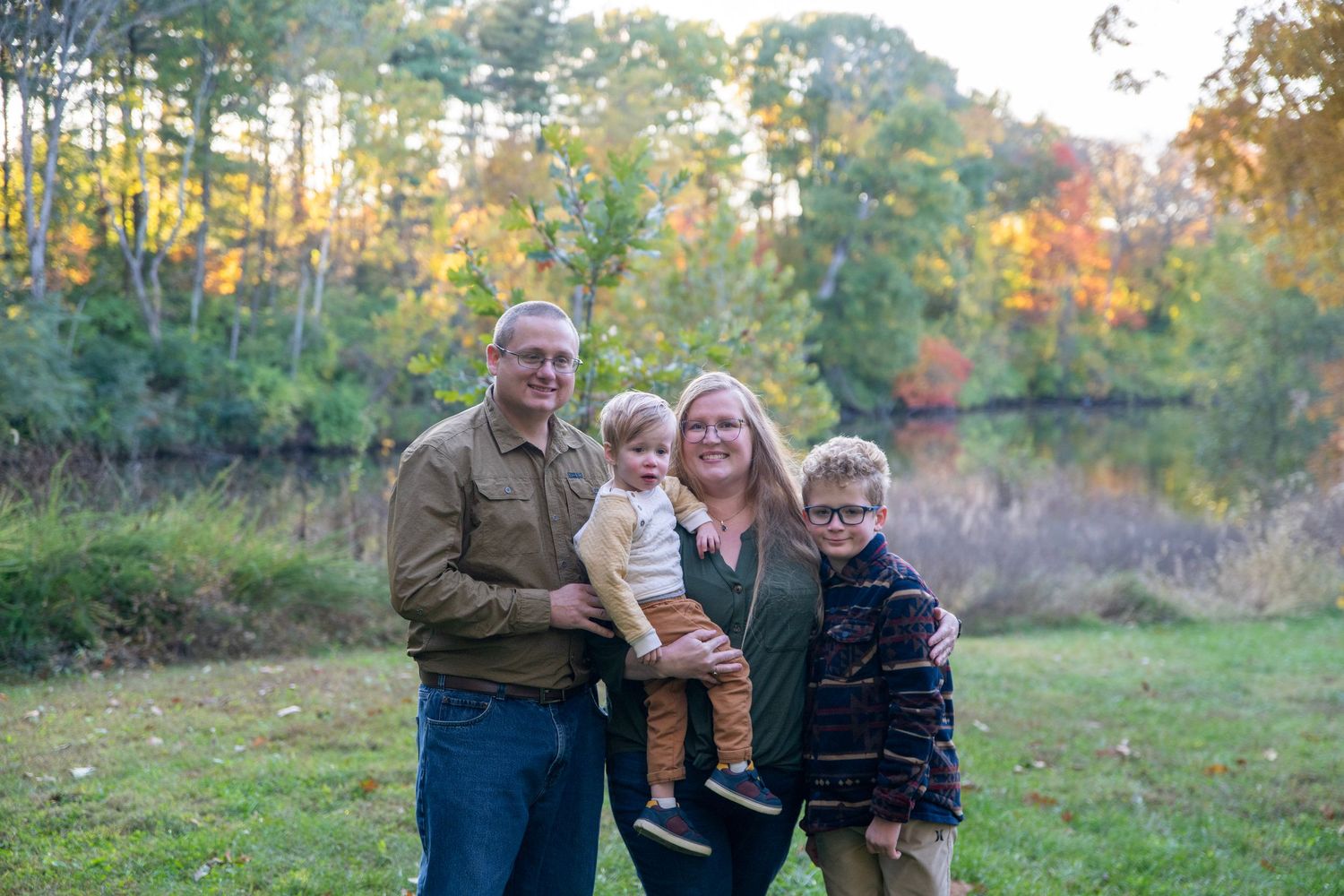 Family members pose together in a natural setting with autumn trees in the background.