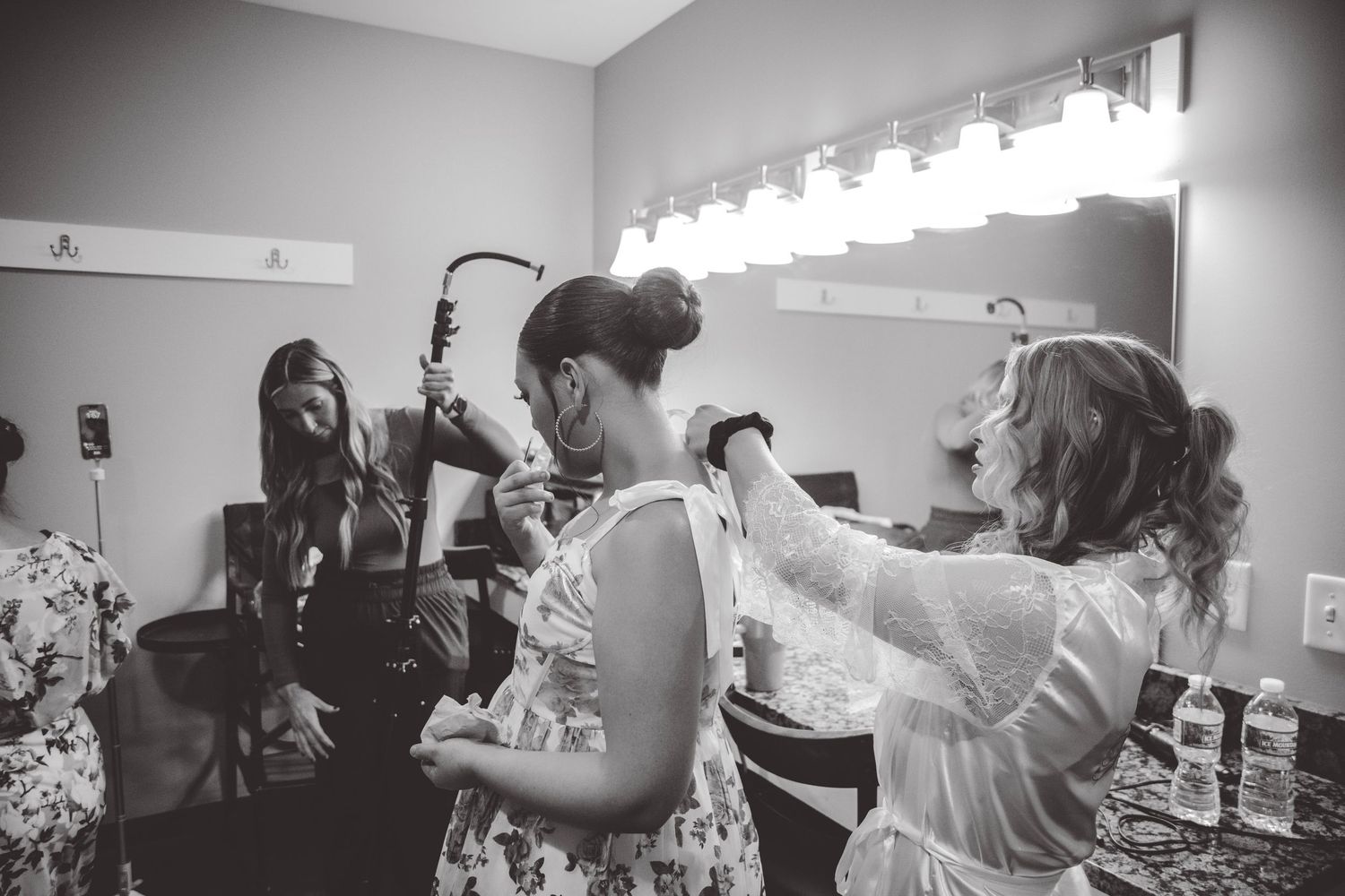 Multiple people assist with wedding day preparations in a brightly lit room.