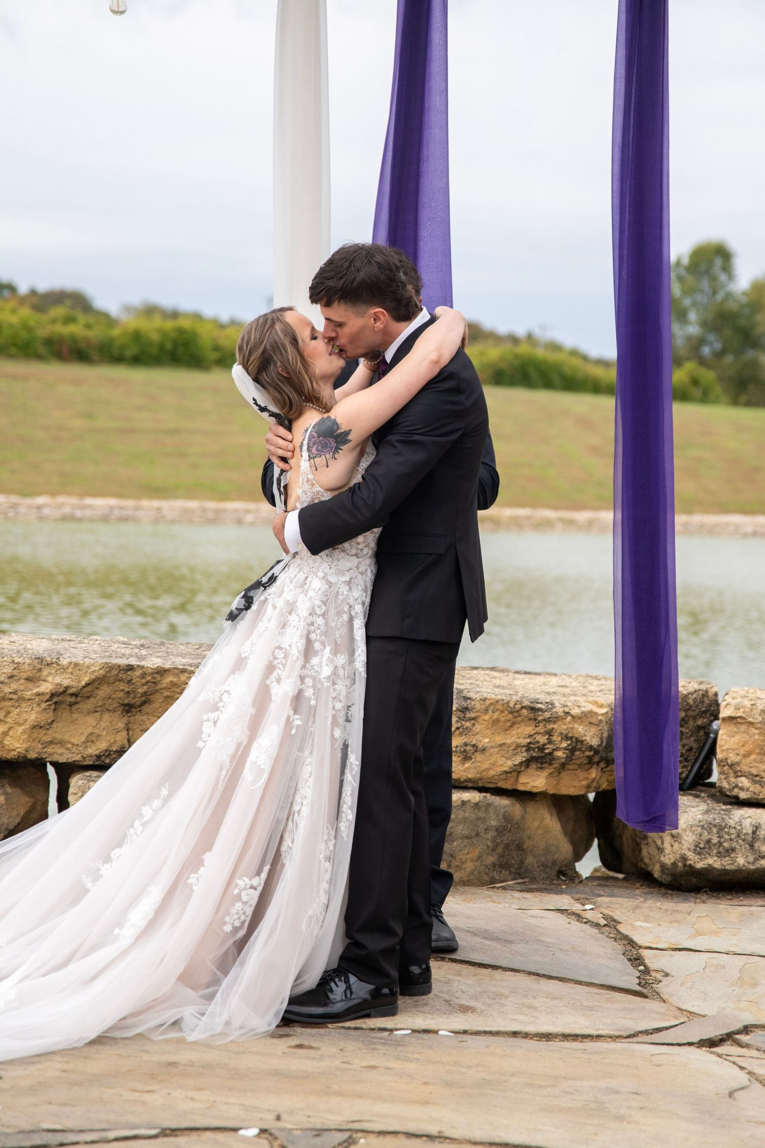 Newlyweds sharing intimate moment under decorated pergola by the lake.