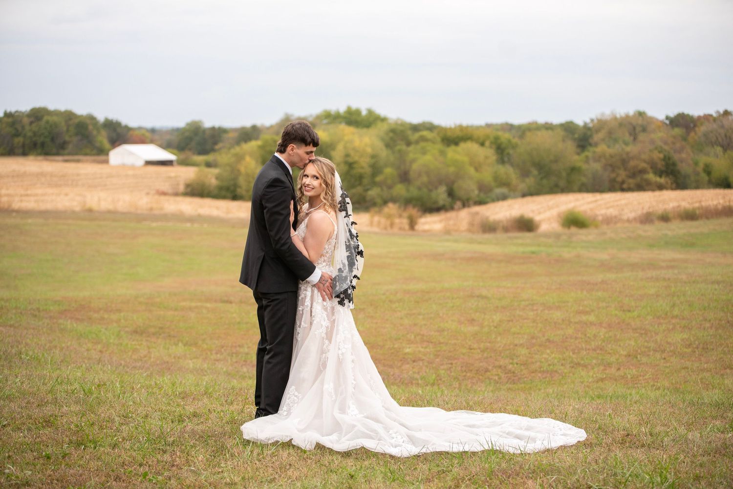 A wedding couple embraces in a rustic outdoor field setting during golden hour.