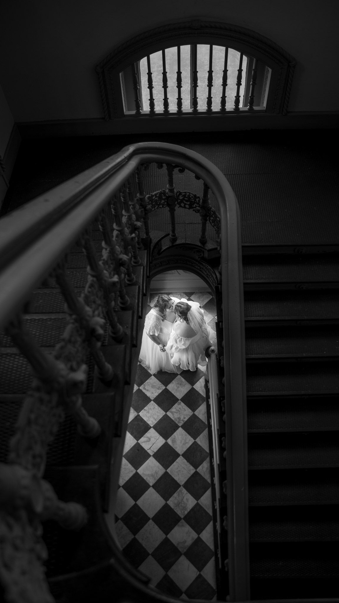 Black and white aerial perspective of two figures in white dresses on a checkered floor.