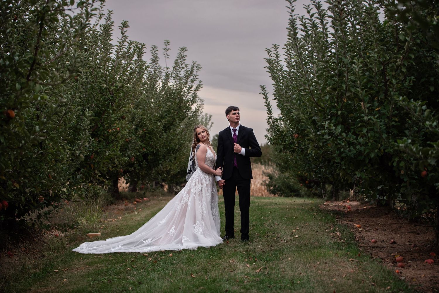 A romantic wedding portrait in an apple orchard with a long white dress trailing behind.