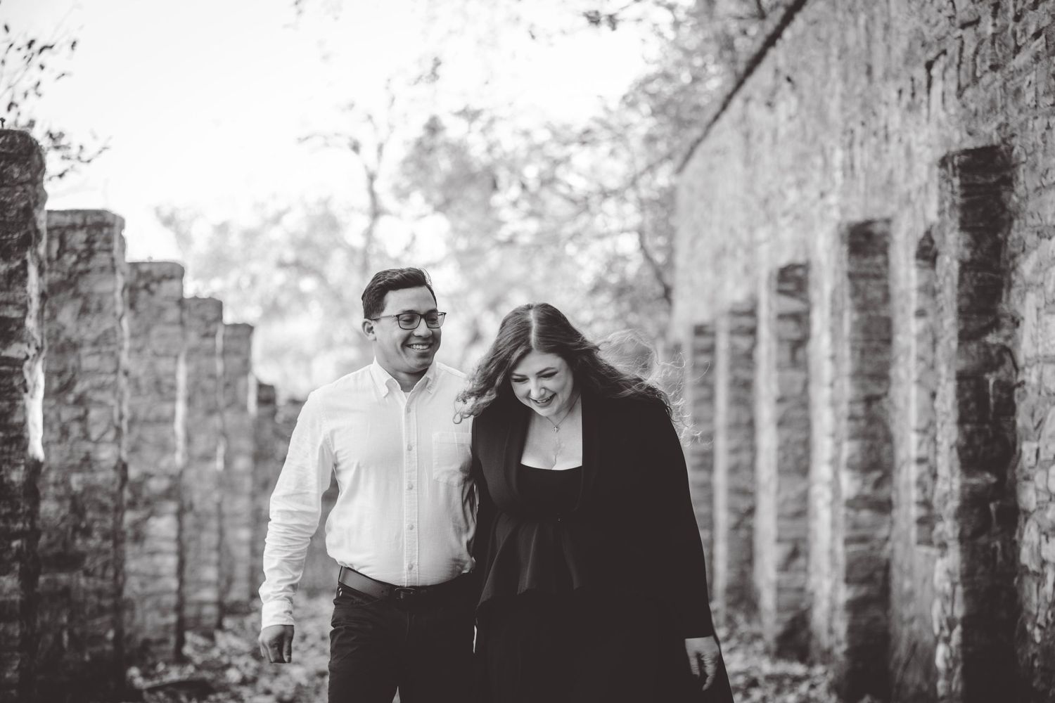 Black and white photo of a couple sharing an intimate moment between stone pillars.