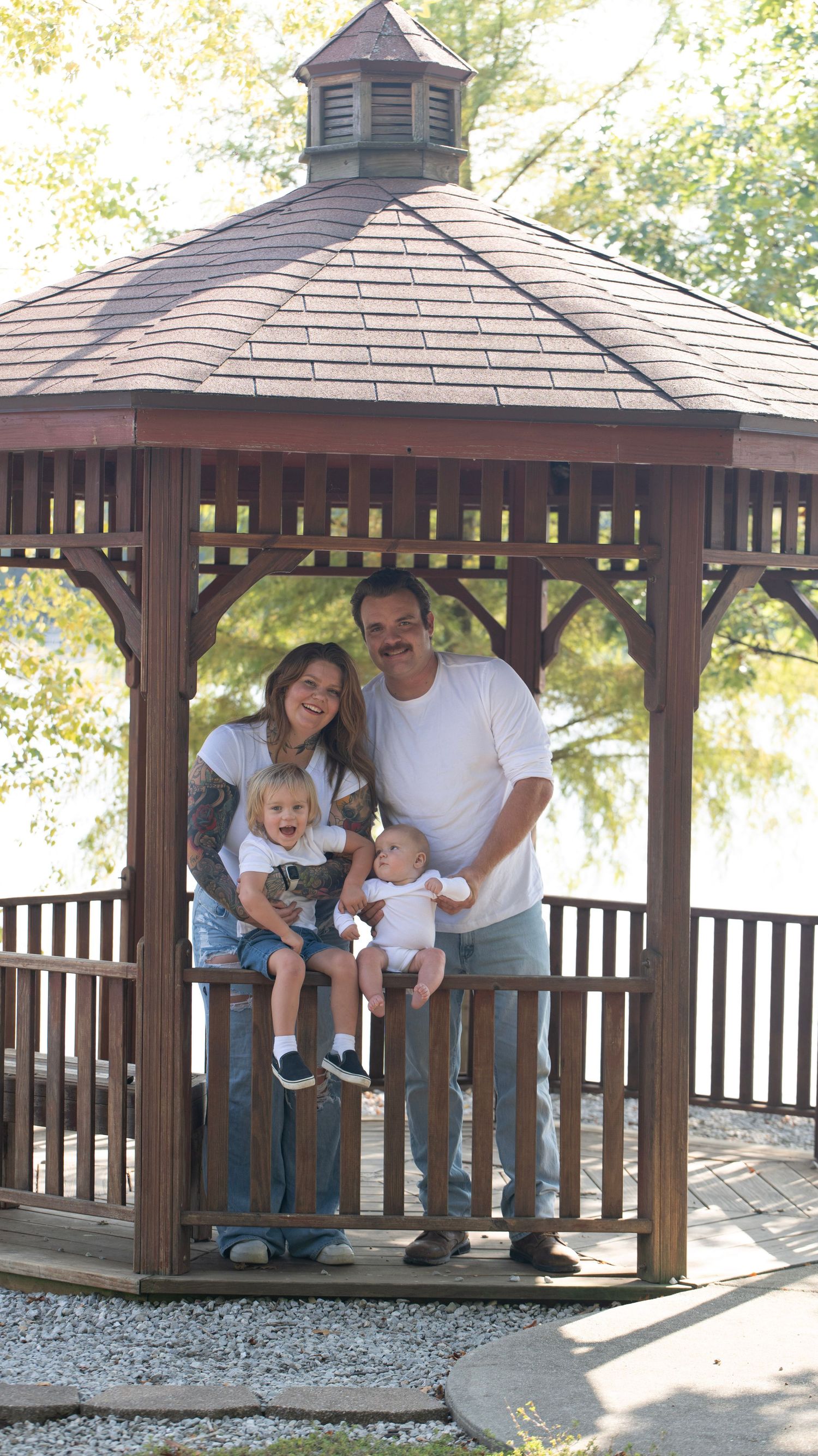 Family enjoying a sunny day together in a wooden gazebo by the water.