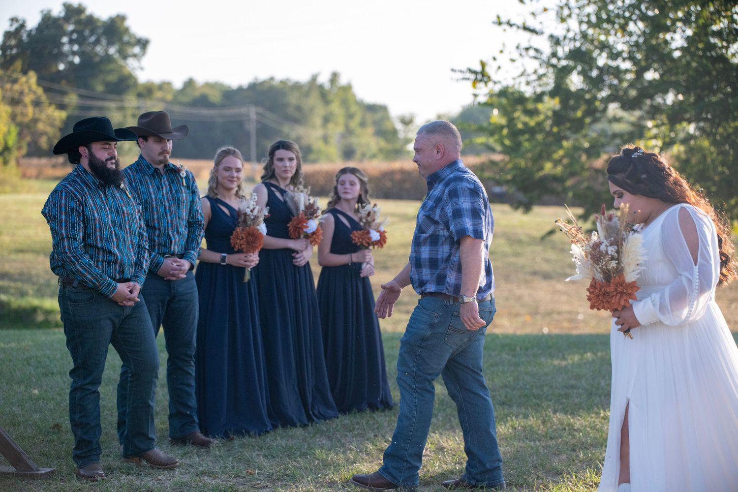 Wedding party and guests lined up outdoors during a country-style ceremony.