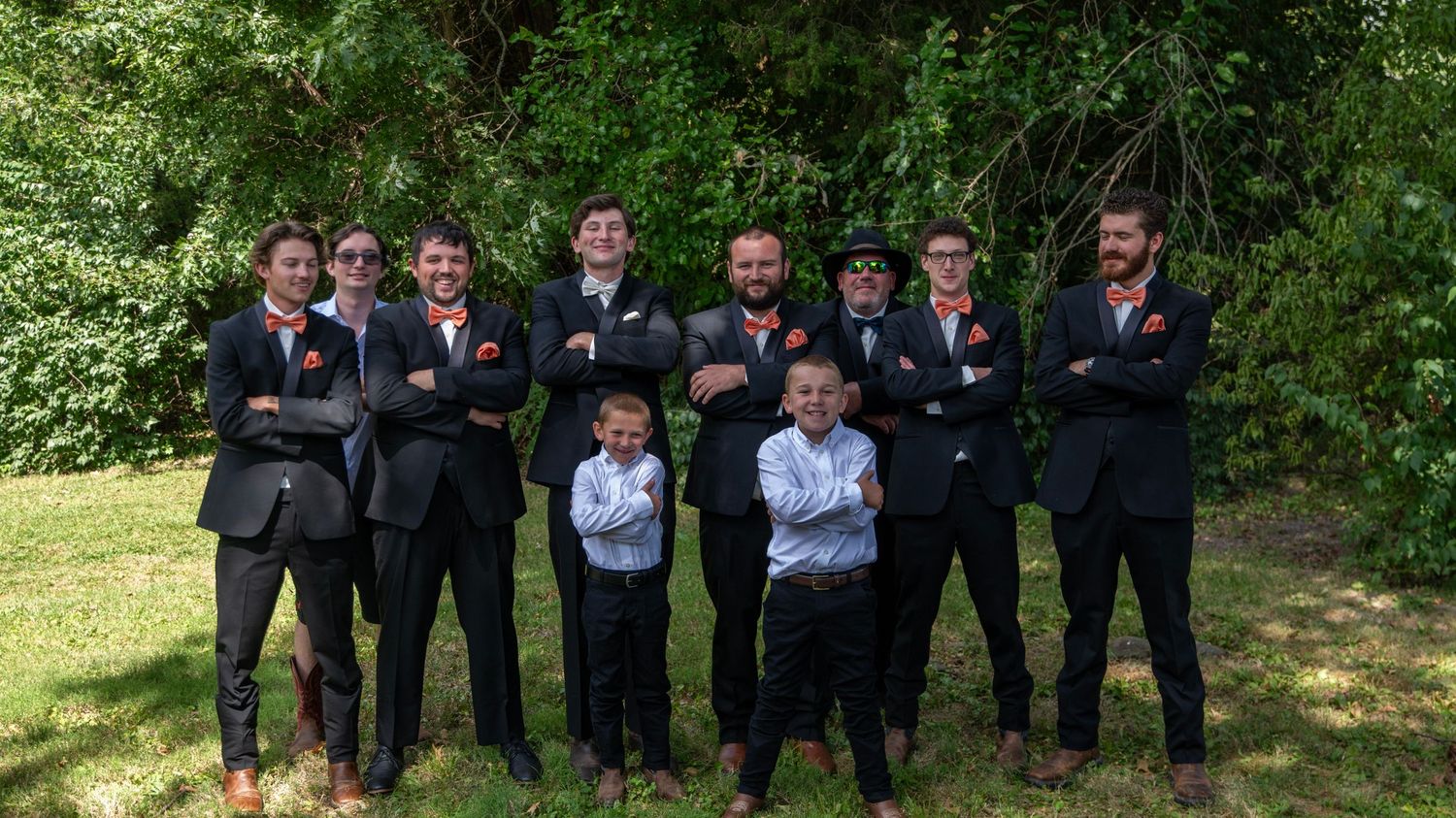 Large wedding party group lined up outdoors with matching formal attire and red accents.