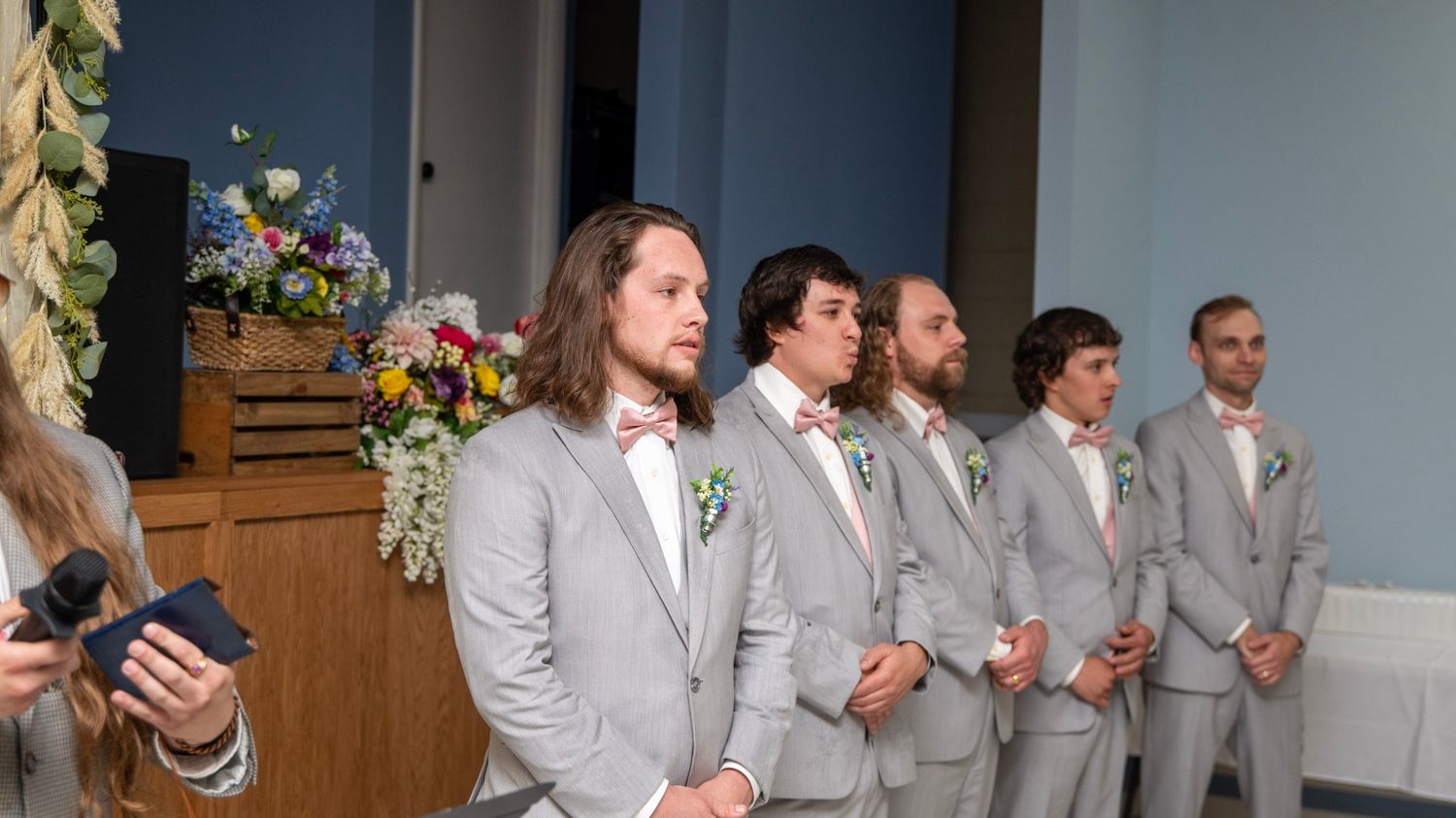 Groomsmen in matching light gray suits stand in line at the altar with floral decorations.