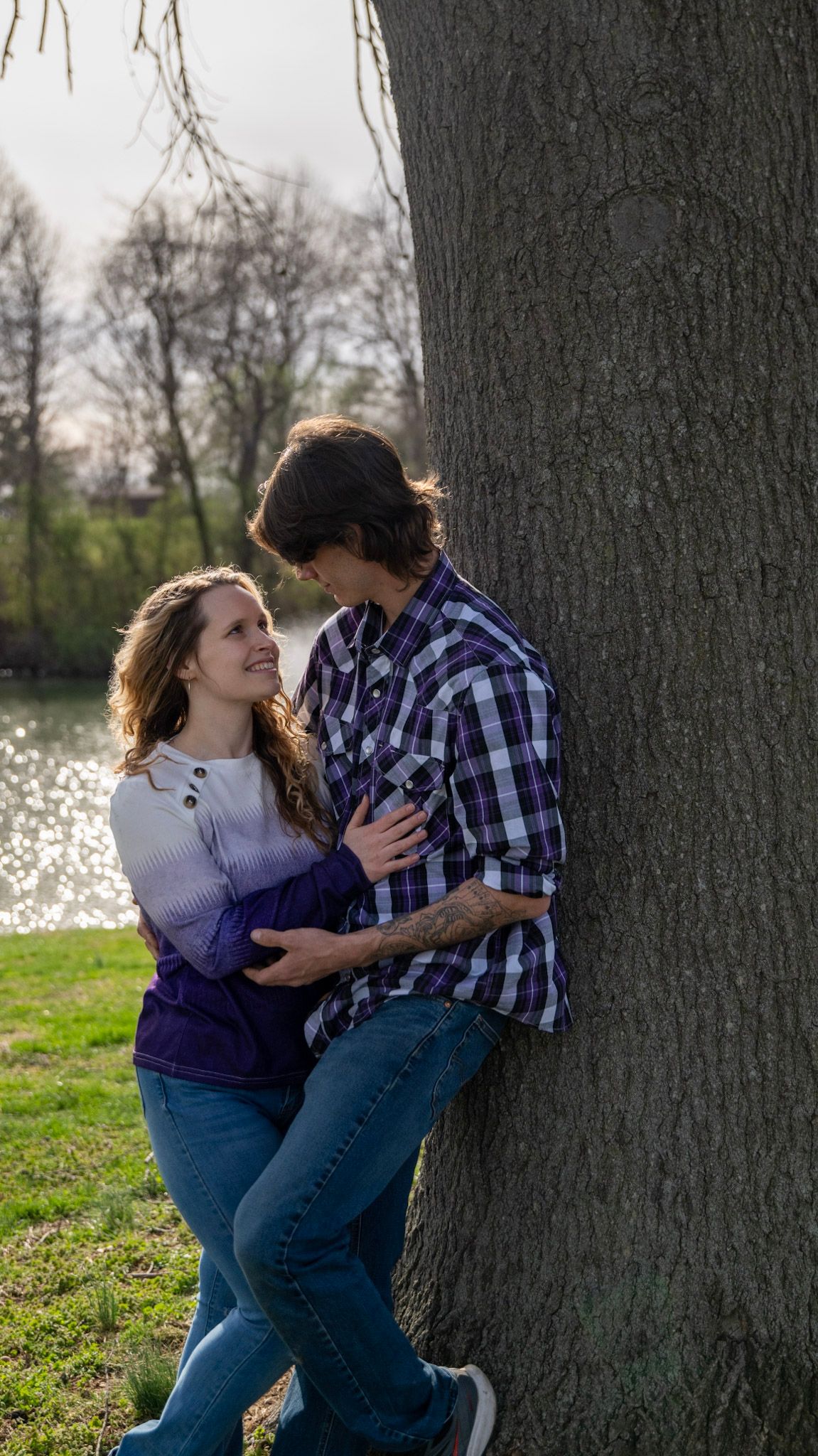 Playful couple sharing a moment against large tree trunks in a park.