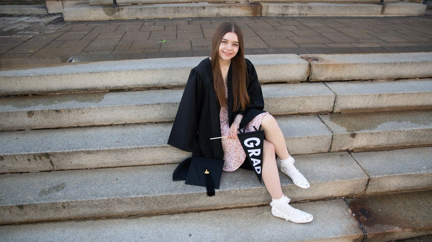 Graduate sitting on stone steps wearing white sneakers and graduation attire.