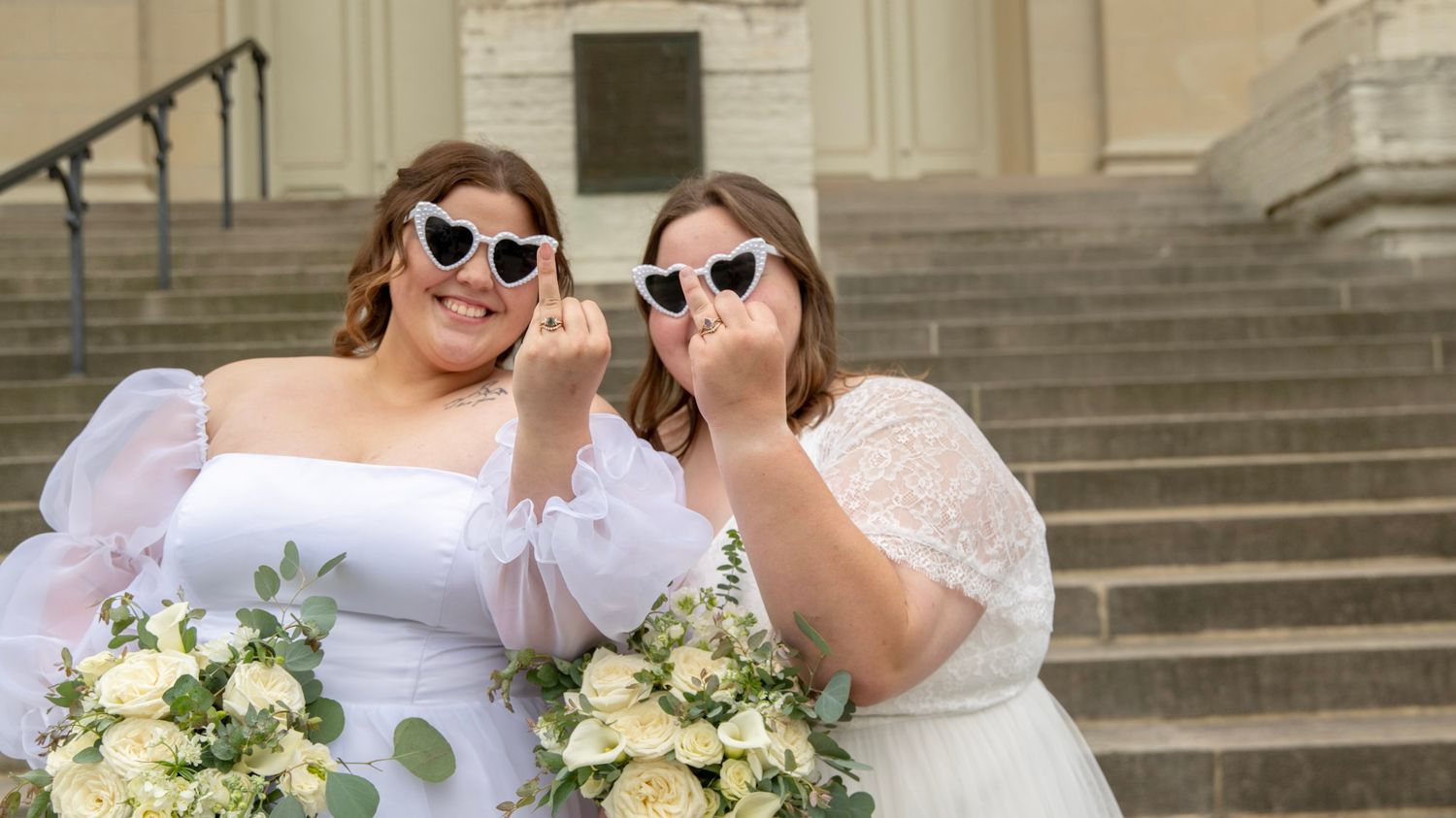 Wedding couple wearing heart-shaped sunglasses pose with bouquets.