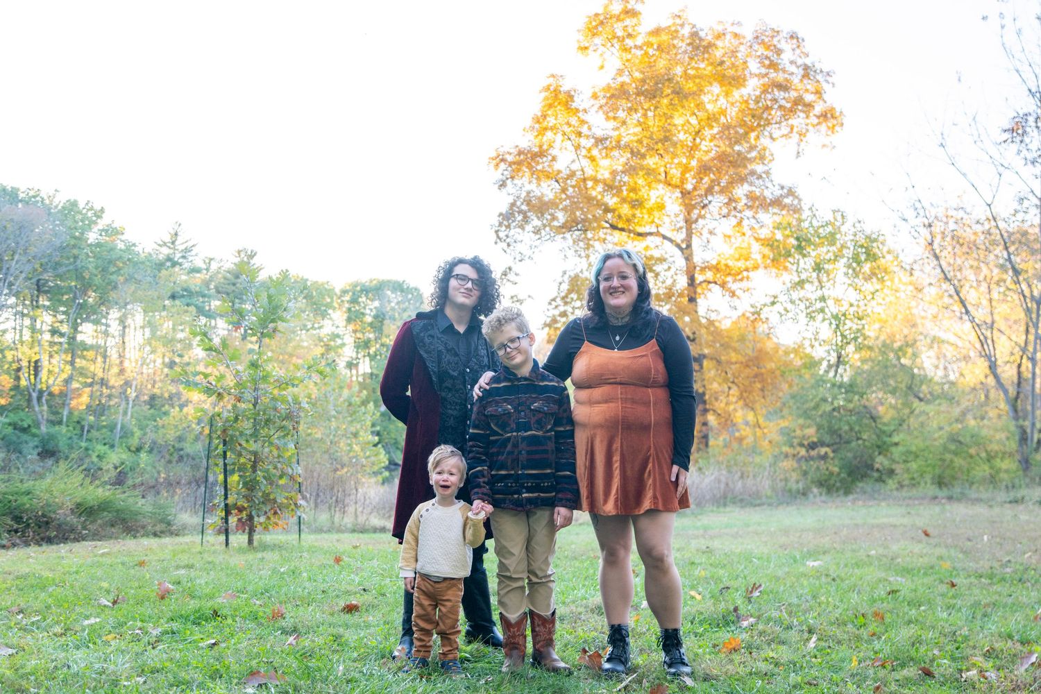 Family group poses together on grassy field with autumn foliage in background.