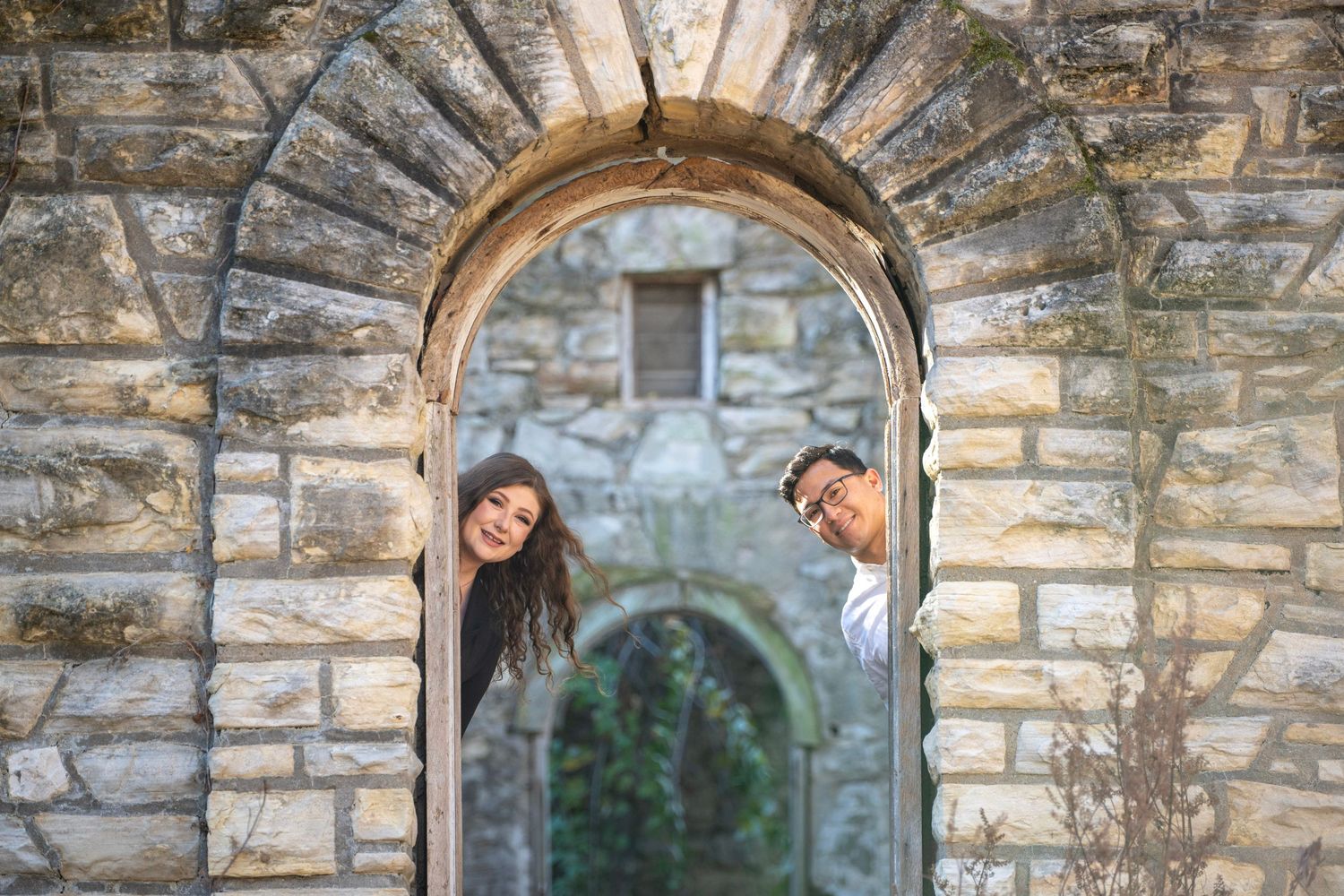 Stone archway frames couple during outdoor photoshoot.