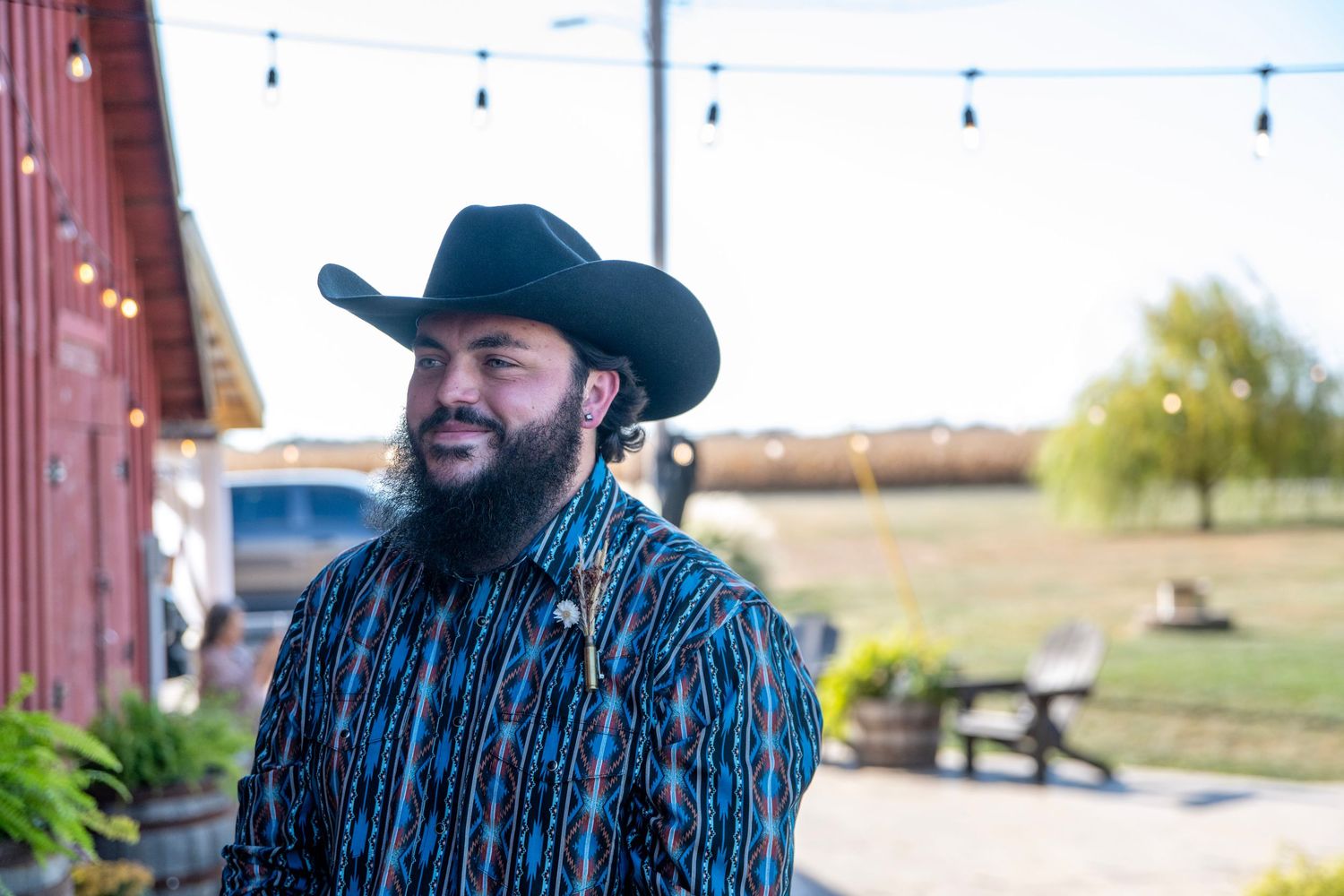 Person in a blue striped shirt and cowboy hat stands outdoors against a rustic barn backdrop.