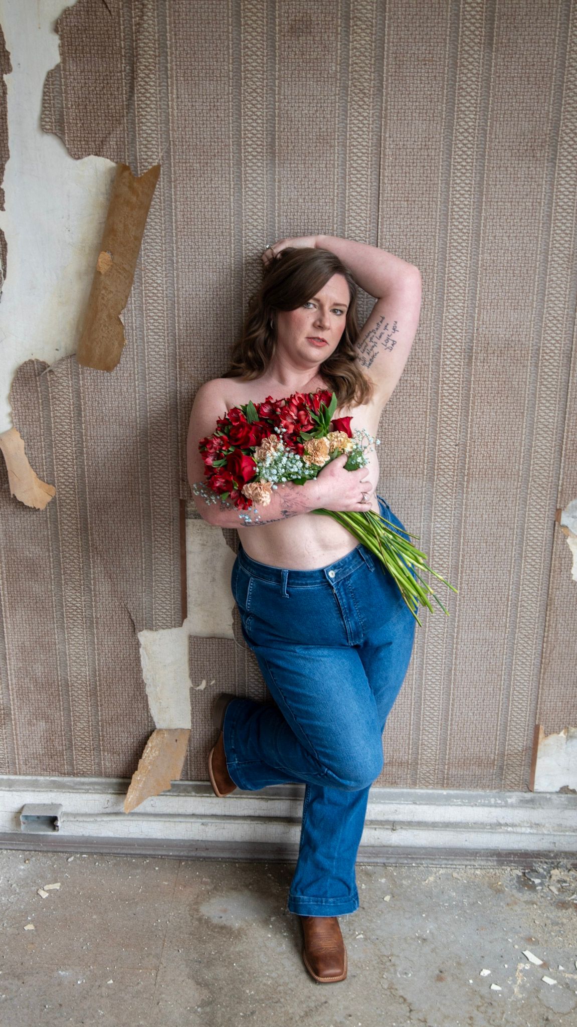 Romantic boudoir portrait with bright red roses against exposed brick wall.
