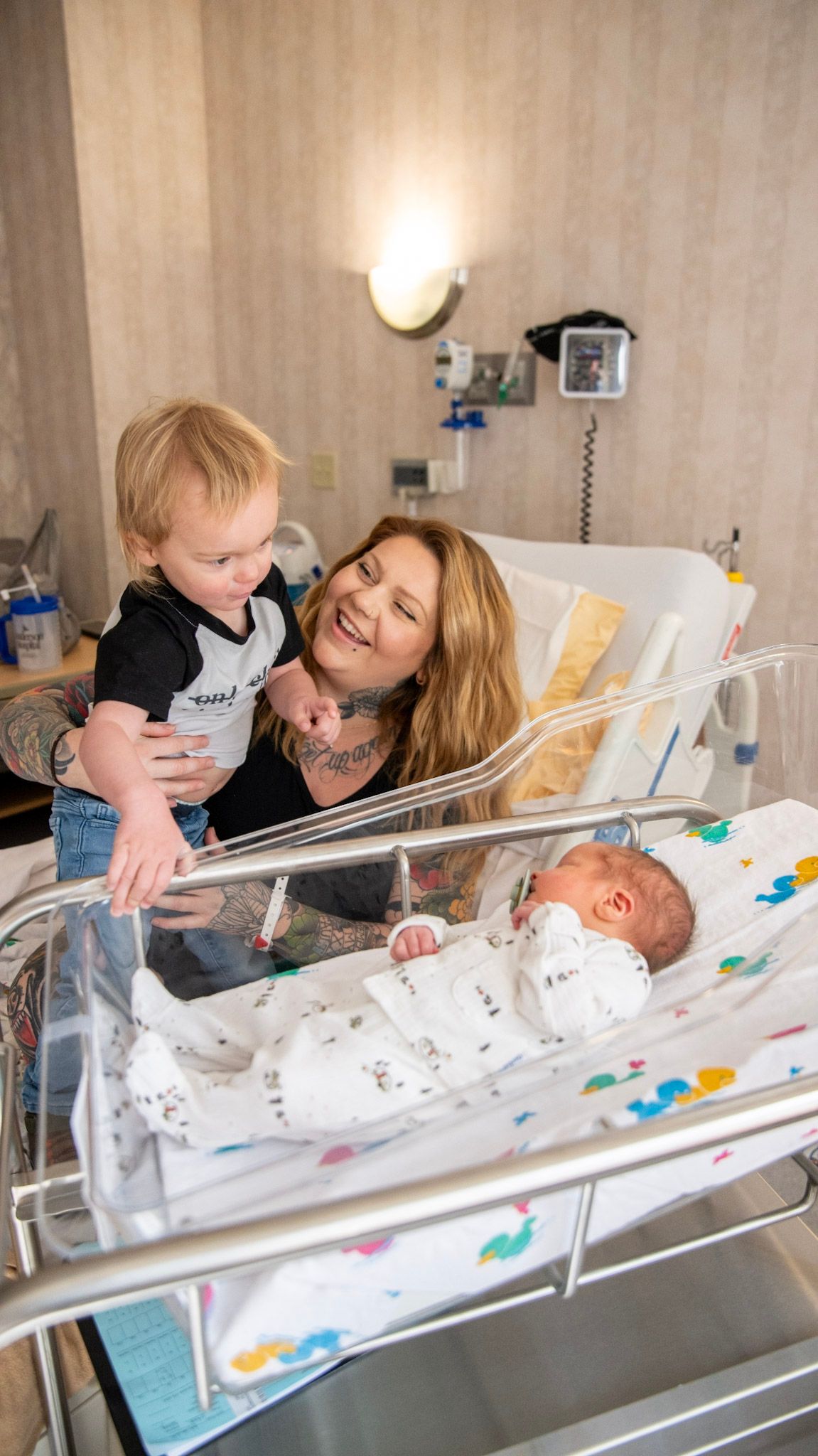 Tender moment in hospital room with newborn in bassinet surrounded by family.