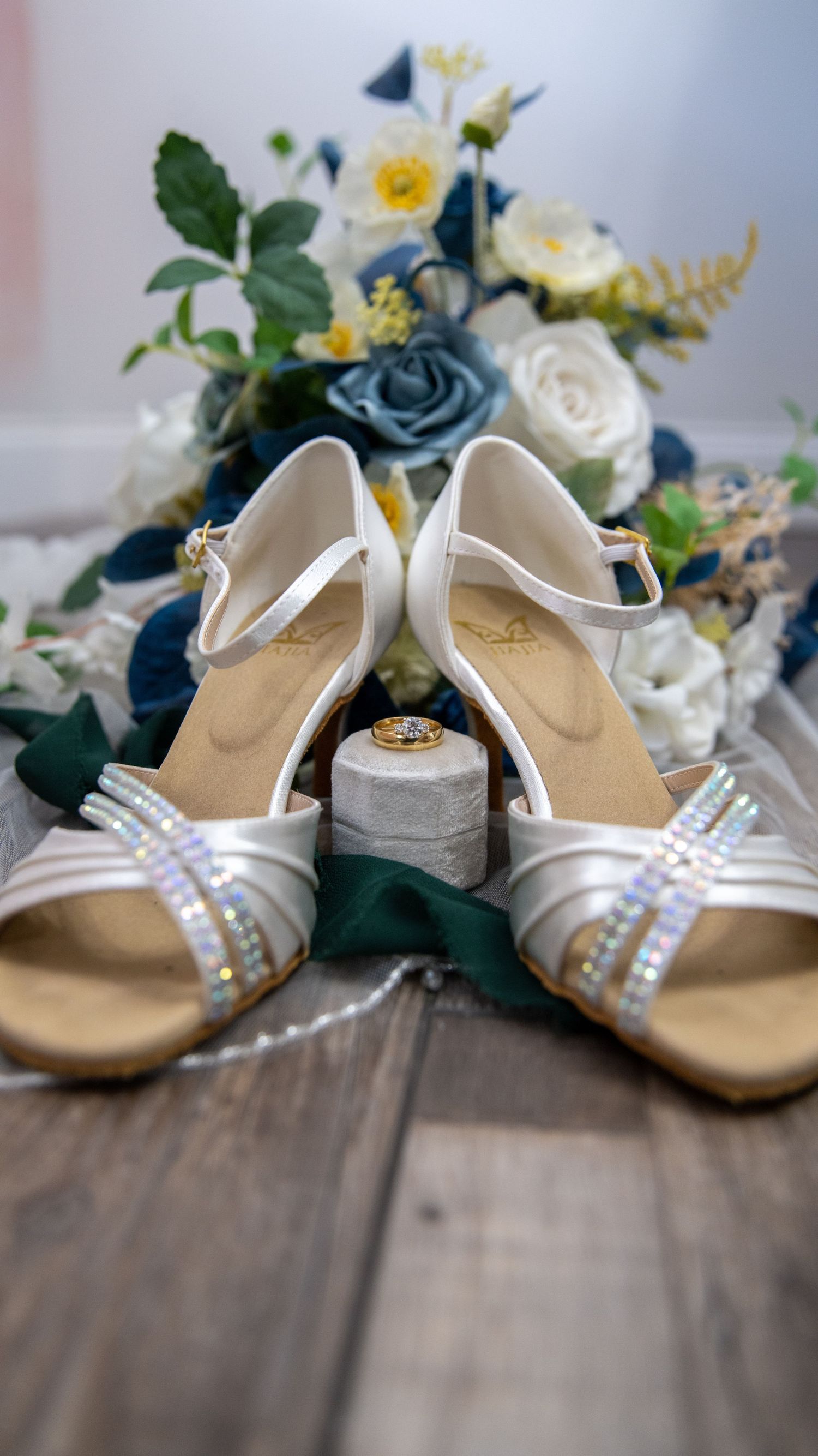 White wedding sandals with pearl details arranged with blue and yellow floral decorations.