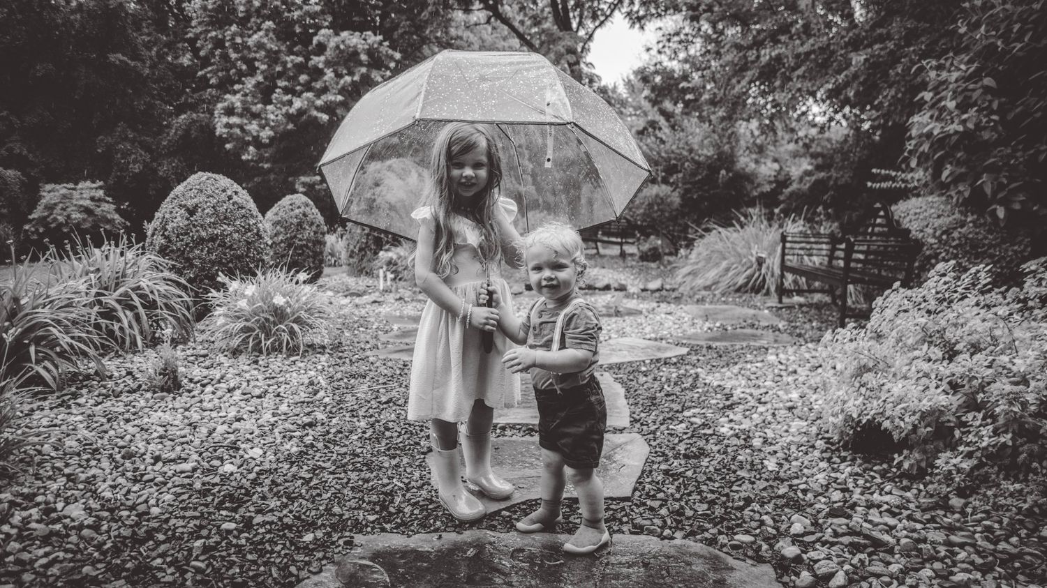 A panoramic black and white view of children with an umbrella in a garden setting.