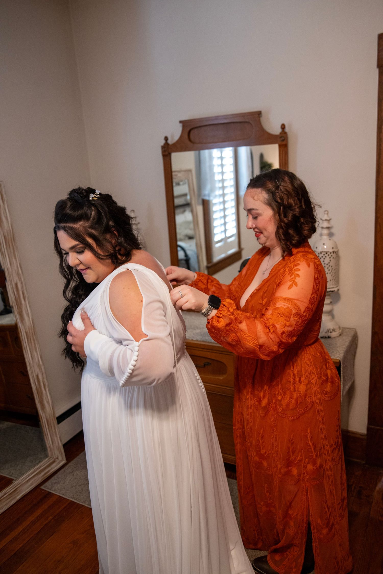Two people helping with dress preparations in indoor setting.