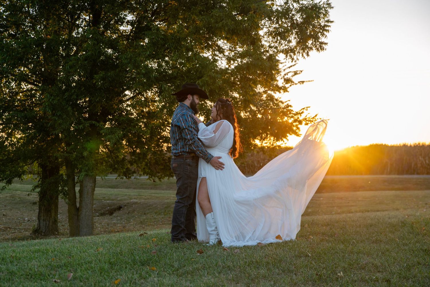 A romantic sunset wedding photo of a couple embracing in a flowing white dress against golden light.