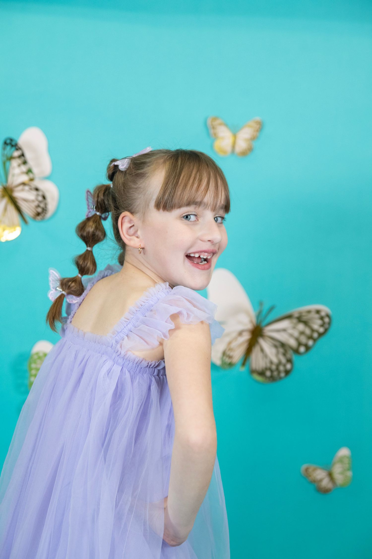 Joyful twirling in a purple tulle dress with butterflies floating against aqua backdrop.