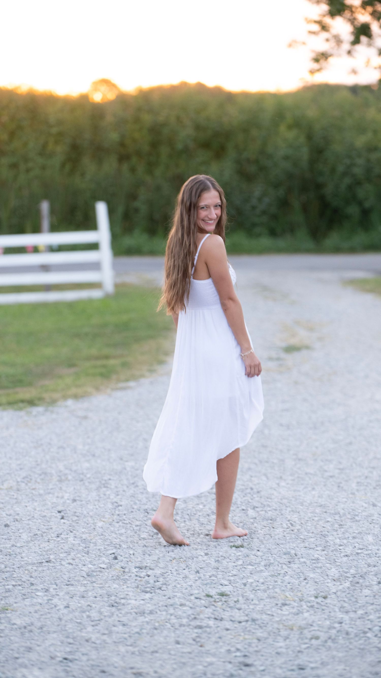Carefree summer portrait on a gravel path wearing a flowing white dress.