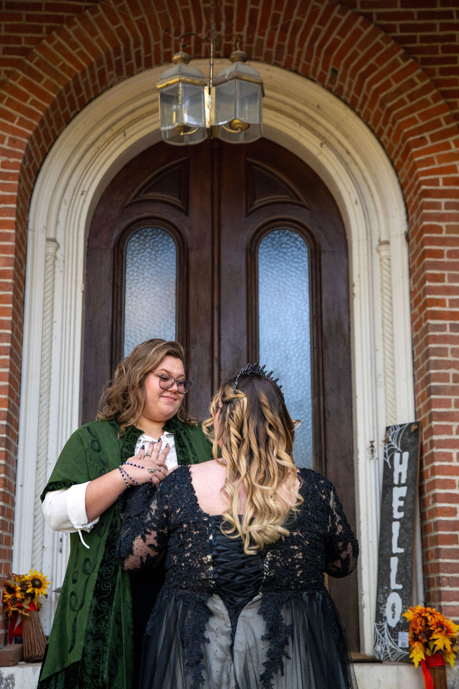 Two people share a joyful moment on a brick building's porch decorated with autumn flowers.
