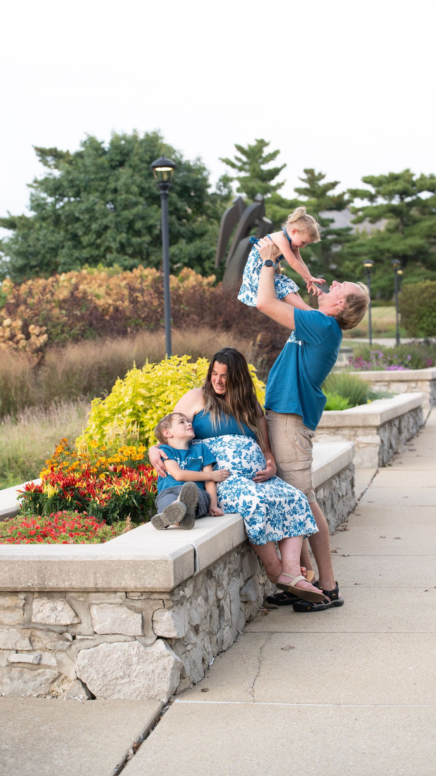 Playful sequence of family interactions on stone wall with colorful garden flowers in background.