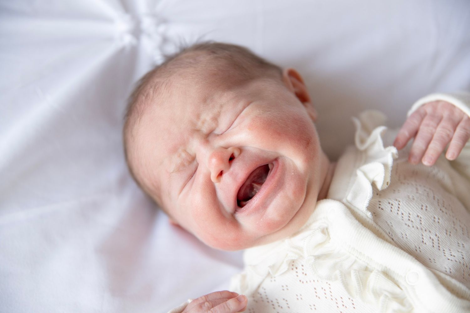 Close-up of sleeping baby in white lace outfit on light bedding.