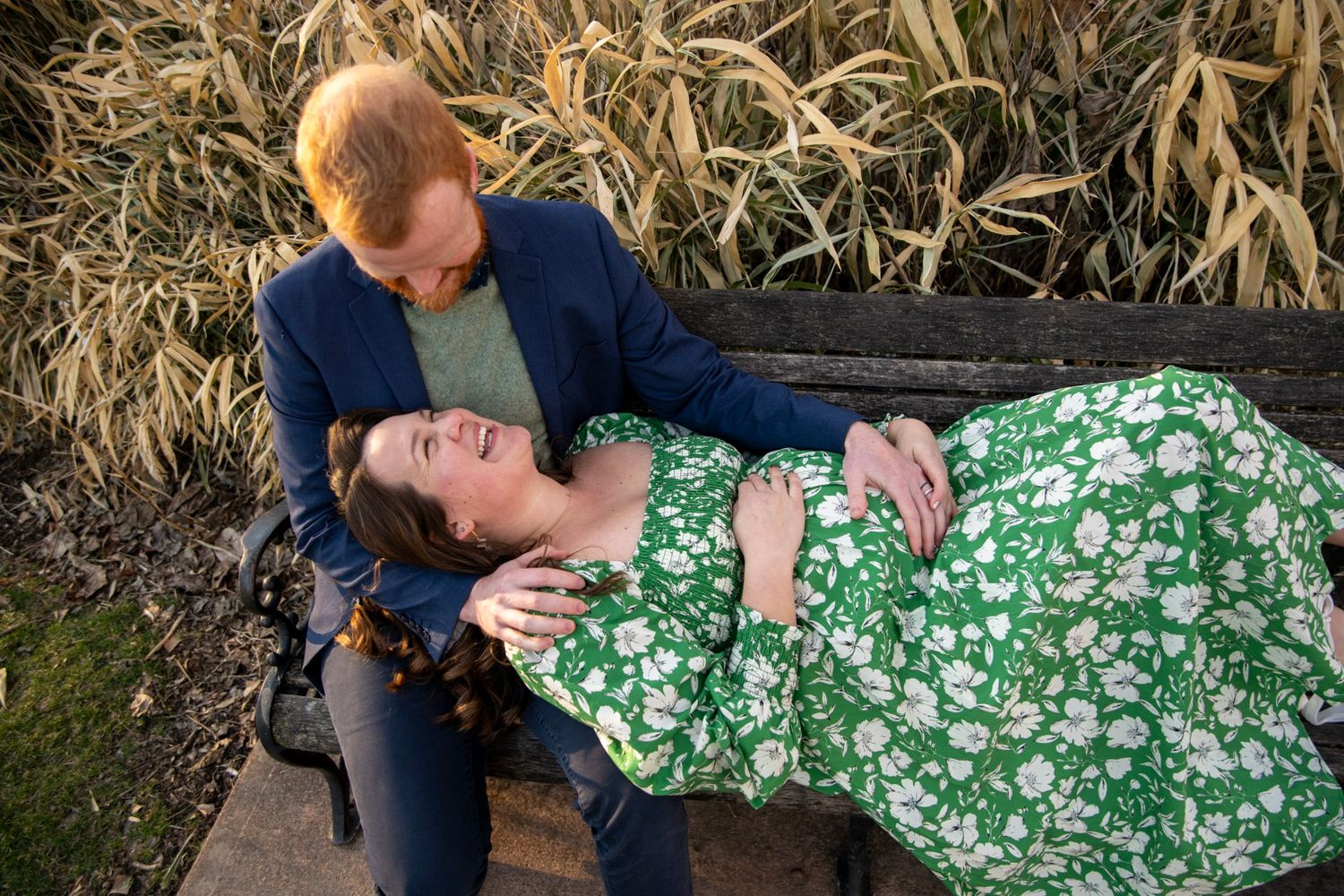 Romantic bench pose with couple in green floral dress and navy suit at golden hour.