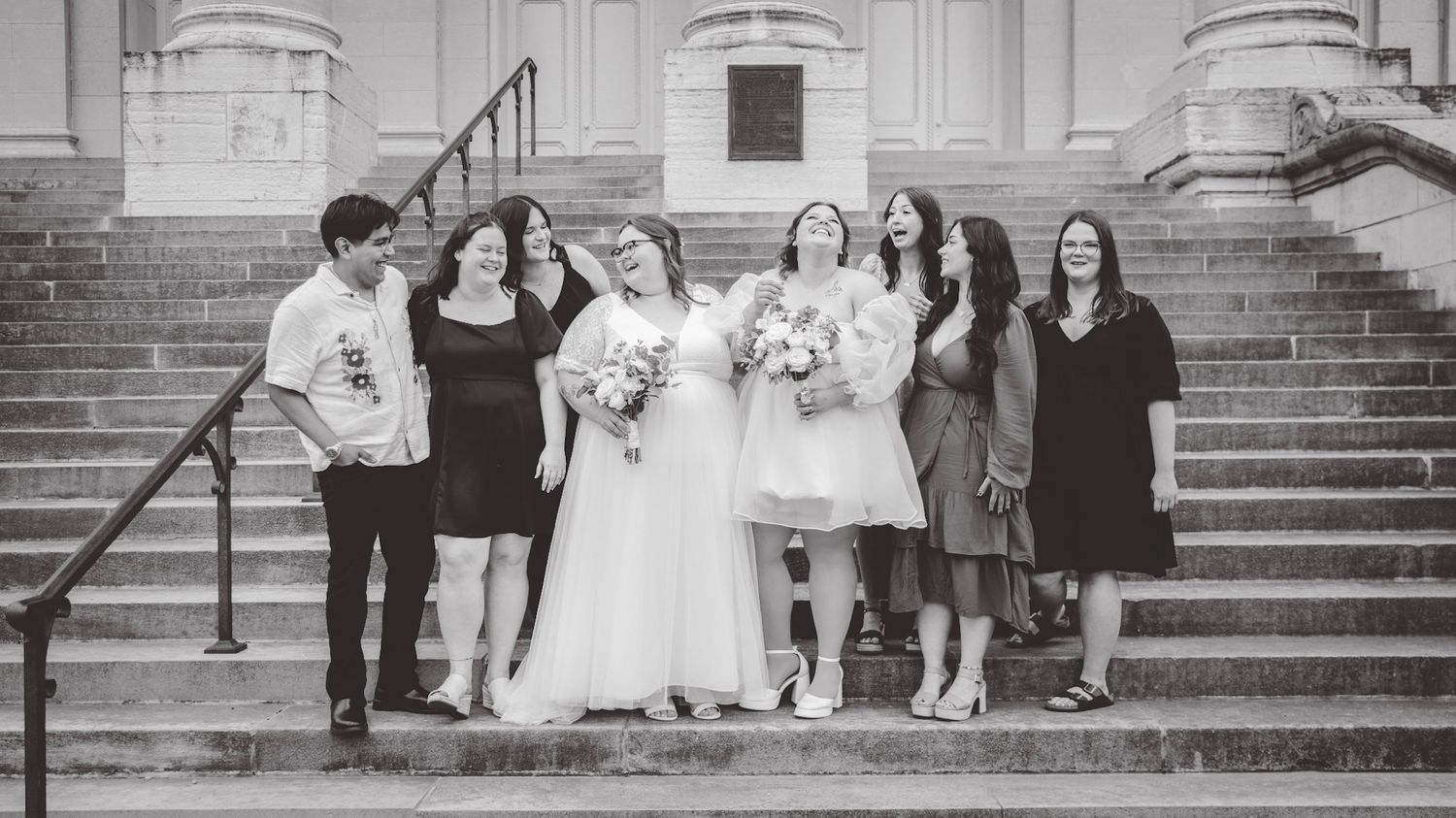 A black and white photo of a wedding party posing together on church steps.