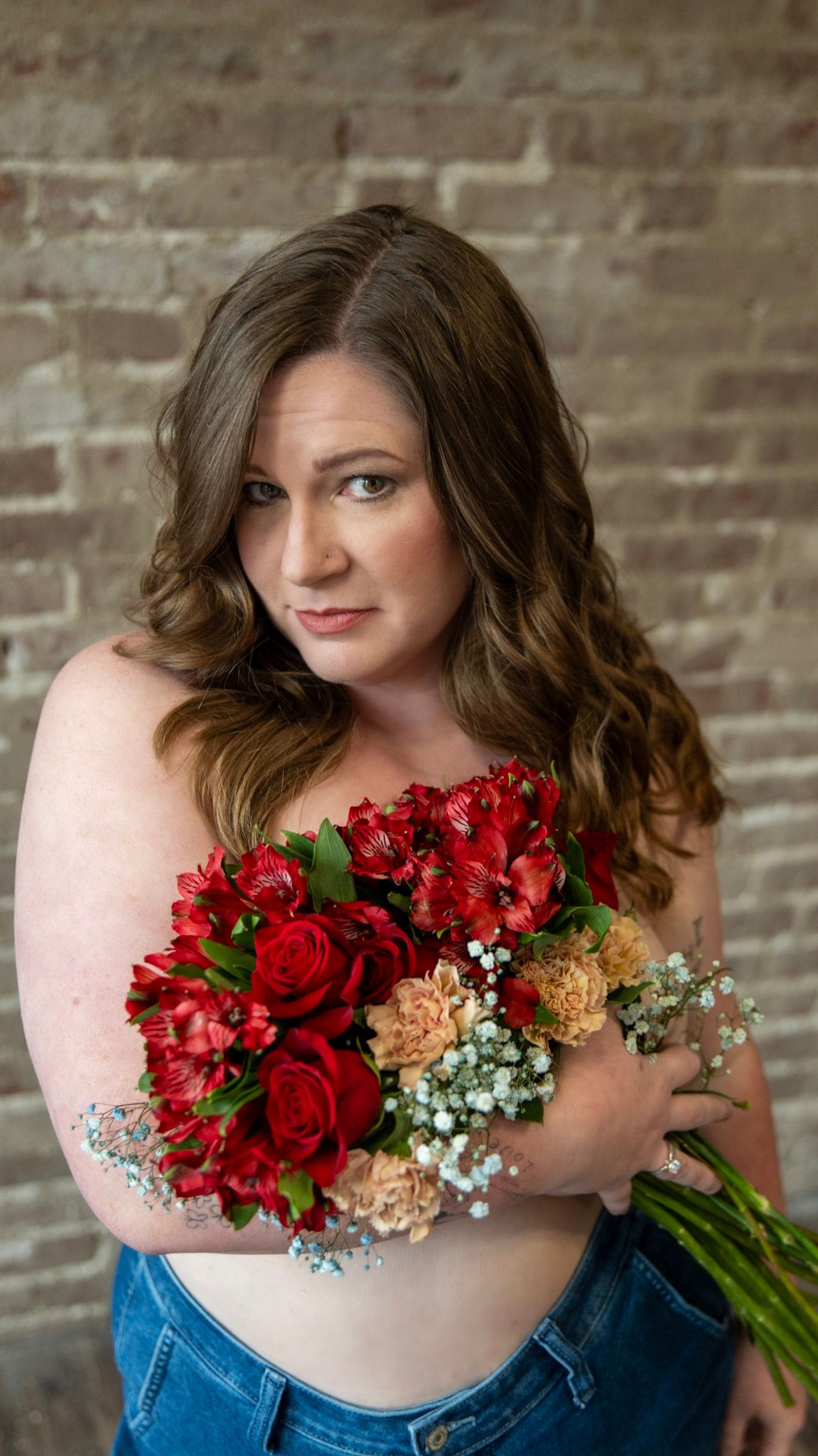 Boudoir portrait with red roses and baby's breath bouquet against brick wall backdrop.