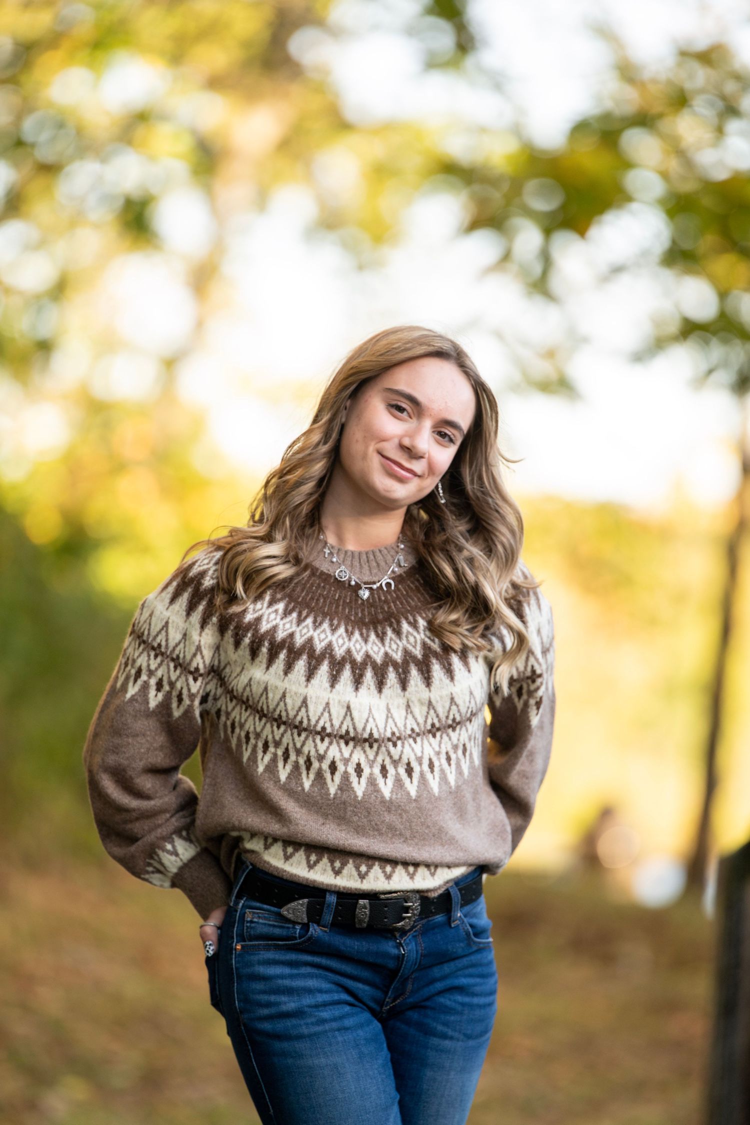 Person in Nordic-style sweater poses outdoors in autumn sunlight.