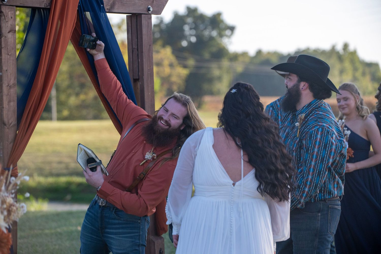 Rustic outdoor wedding ceremony with wooden arch and guests in attendance.