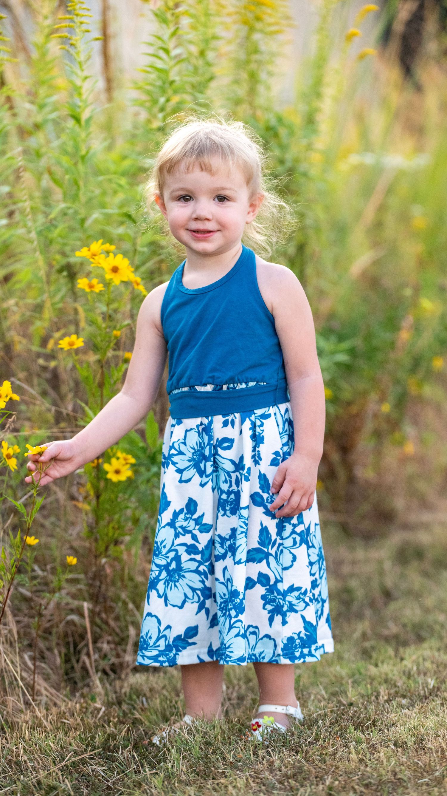 Child in blue and white patterned dress playing among yellow wildflowers.