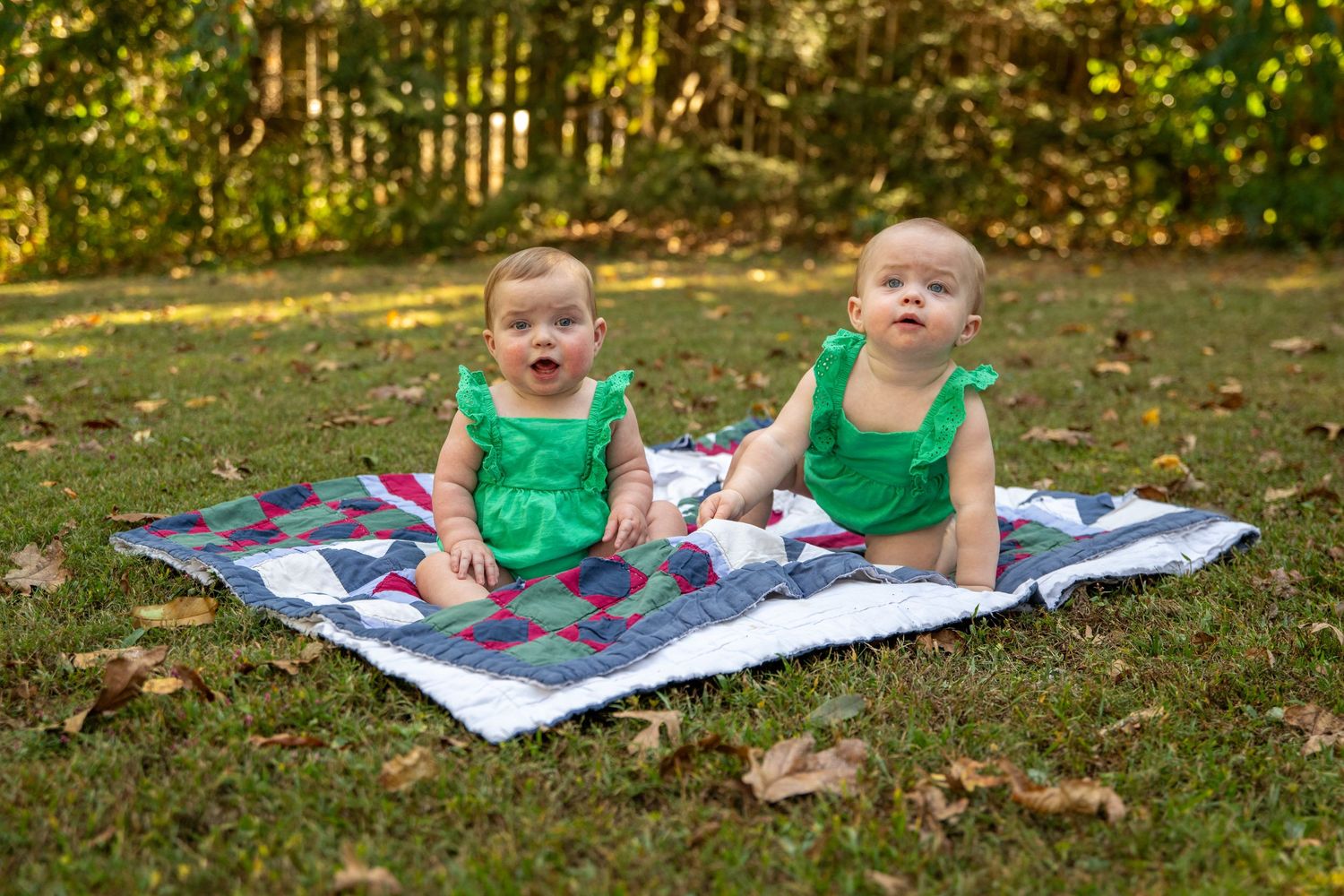 Baby sitting on geometric print blanket in sunny backyard garden setting.