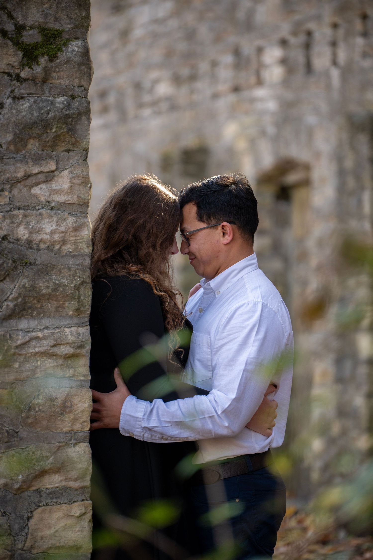 A romantic embrace captured between stone columns in an autumn garden setting.