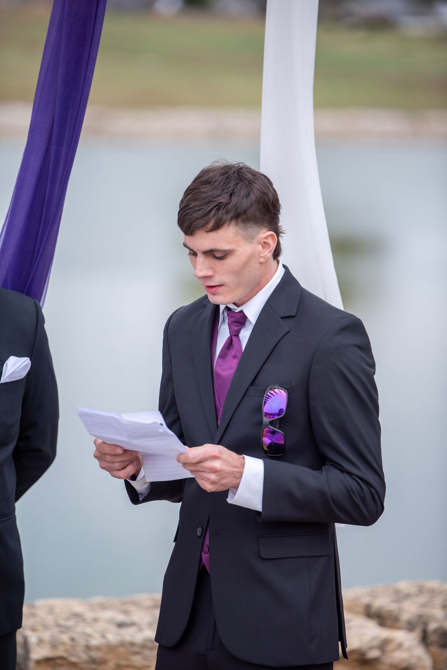 Person reading from paper during outdoor wedding ceremony with purple decor.