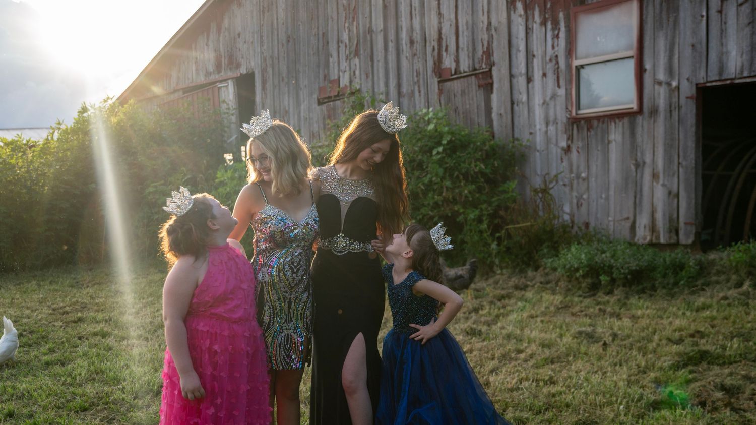 Multiple figures in flowing dresses pose near an old barn during golden hour.