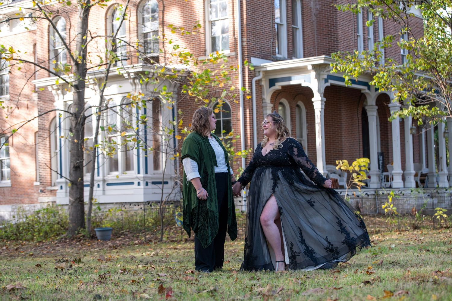 People in dark clothing pose against a historic brick mansion during fall.