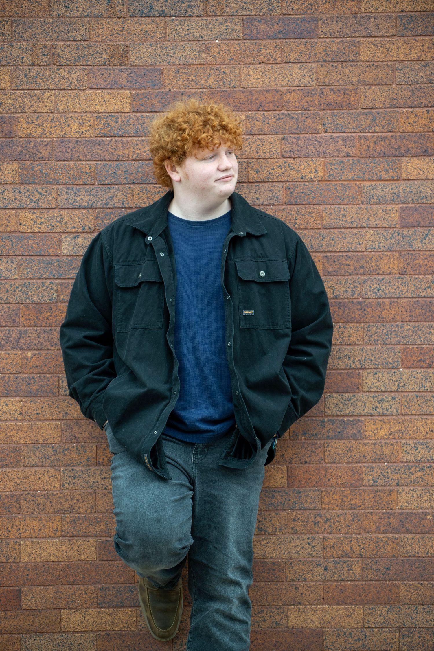 Portrait series against a brick wall showing casual poses in dark jacket and jeans.