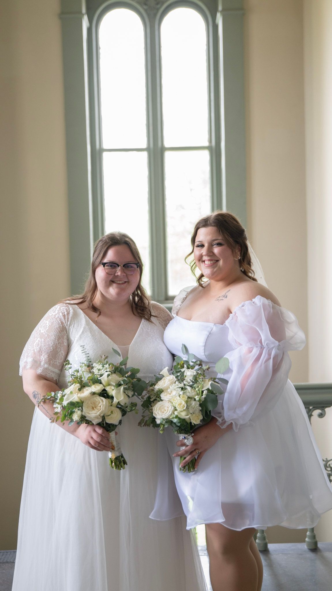 Wedding party in white dresses posing by bright windows in an elegant venue.