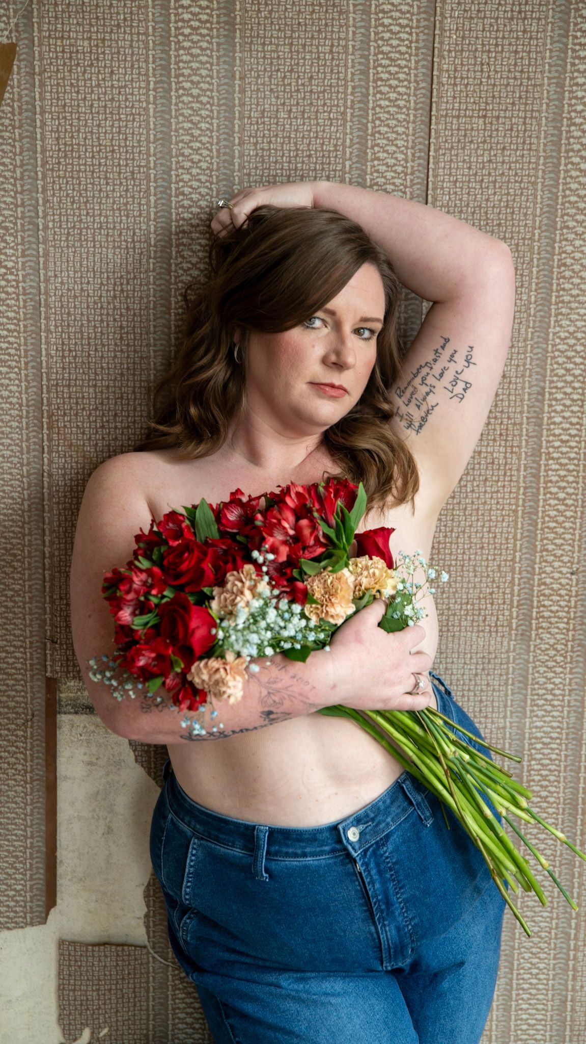 Artistic pose against textured wall with vibrant red and peach floral arrangement.
