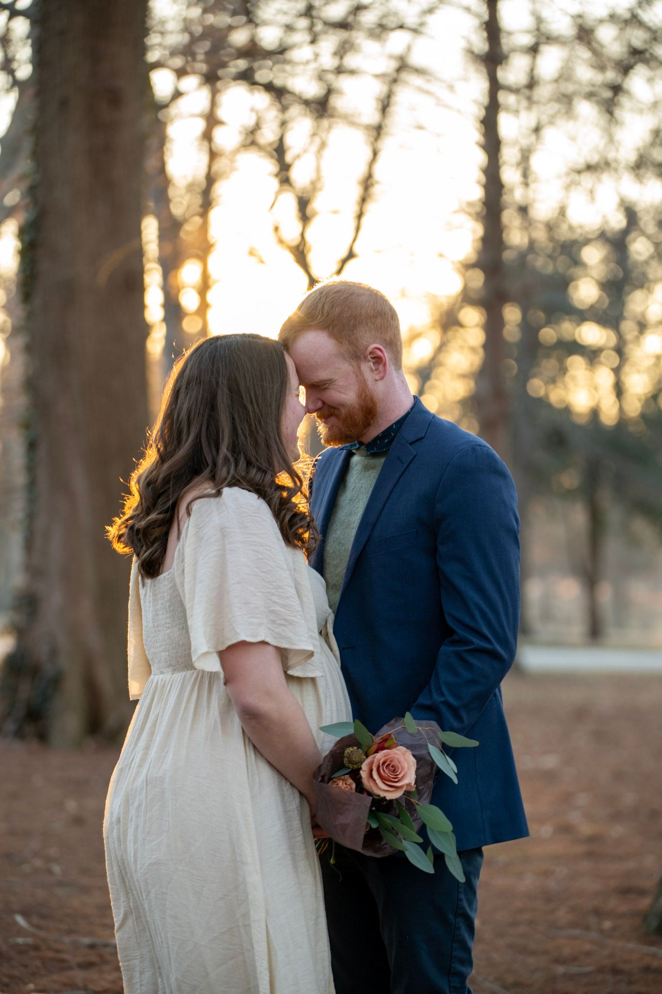 Couple shares tender moment in forest setting during golden hour.