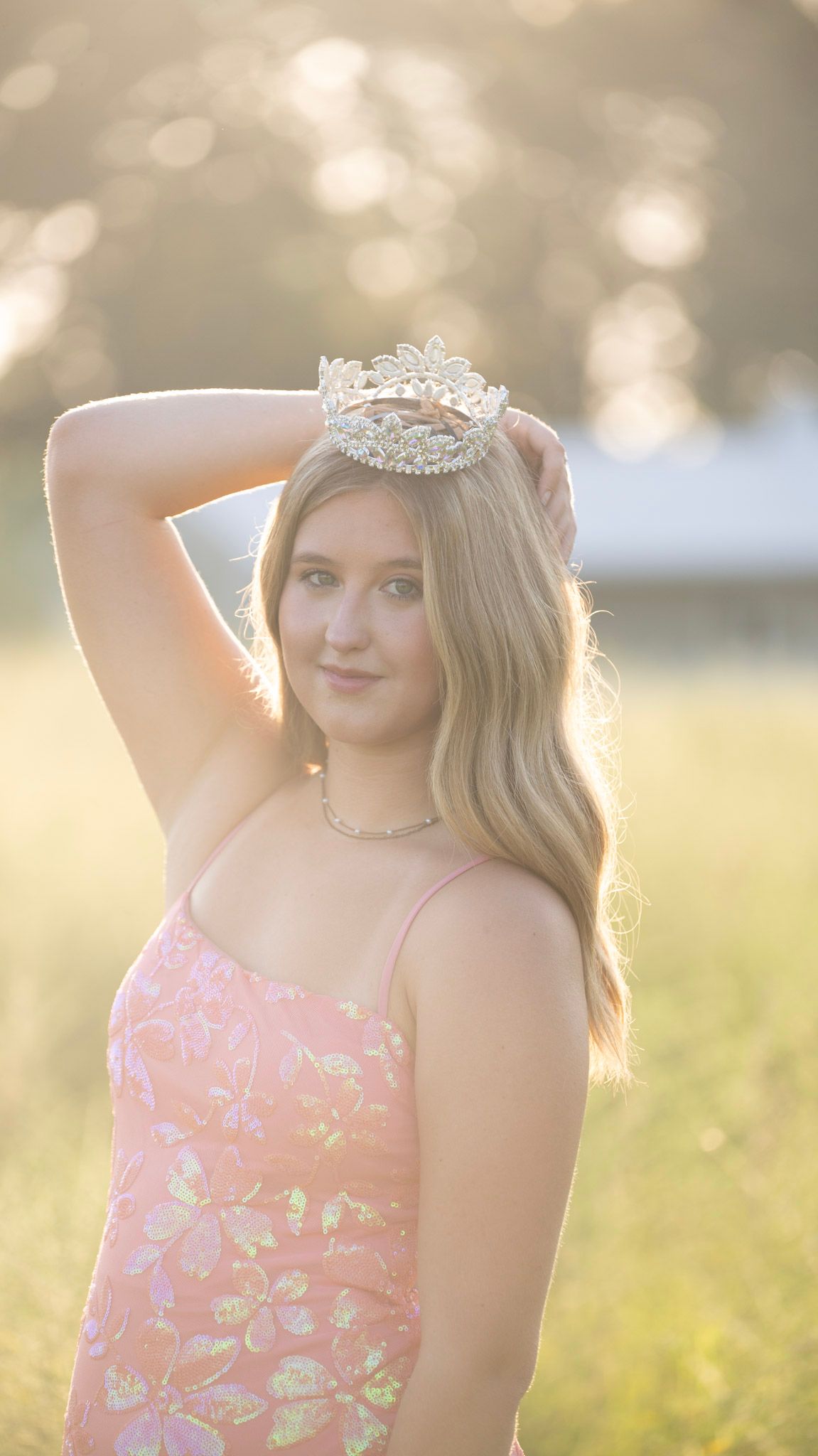 Elegant formal portrait against a sunlit natural background with a delicate tiara.