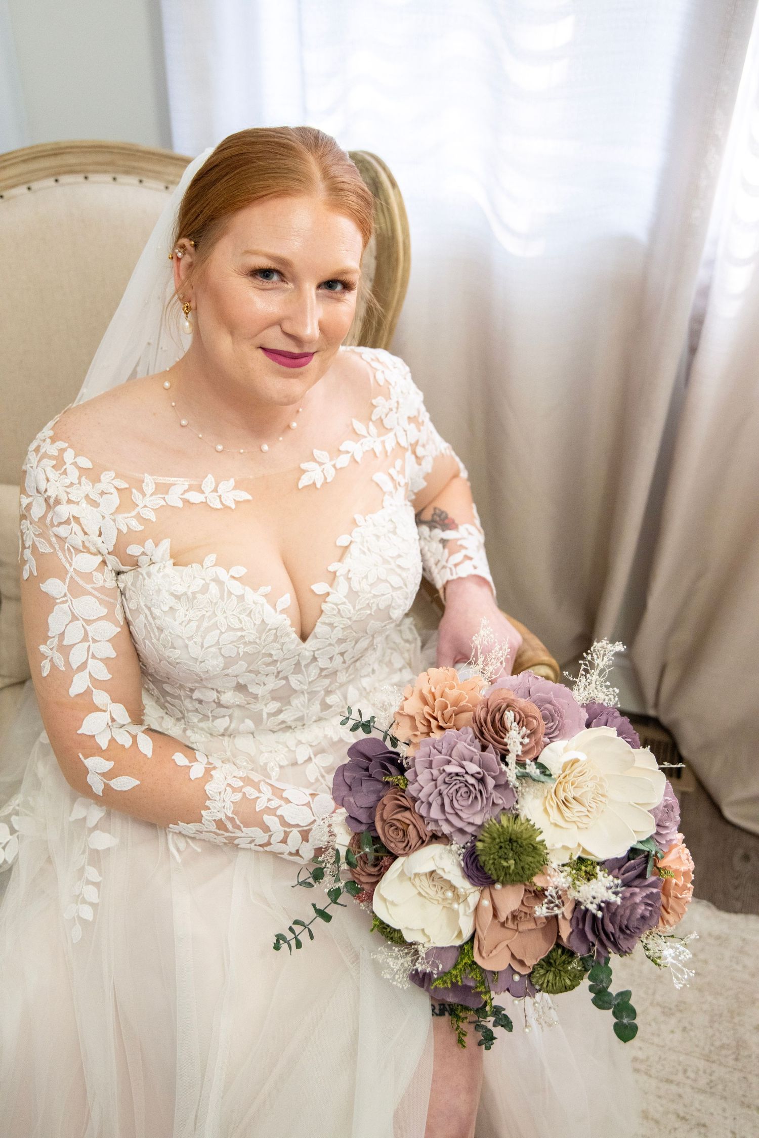 Wedding dress details with delicate lace overlay and purple floral bouquet.