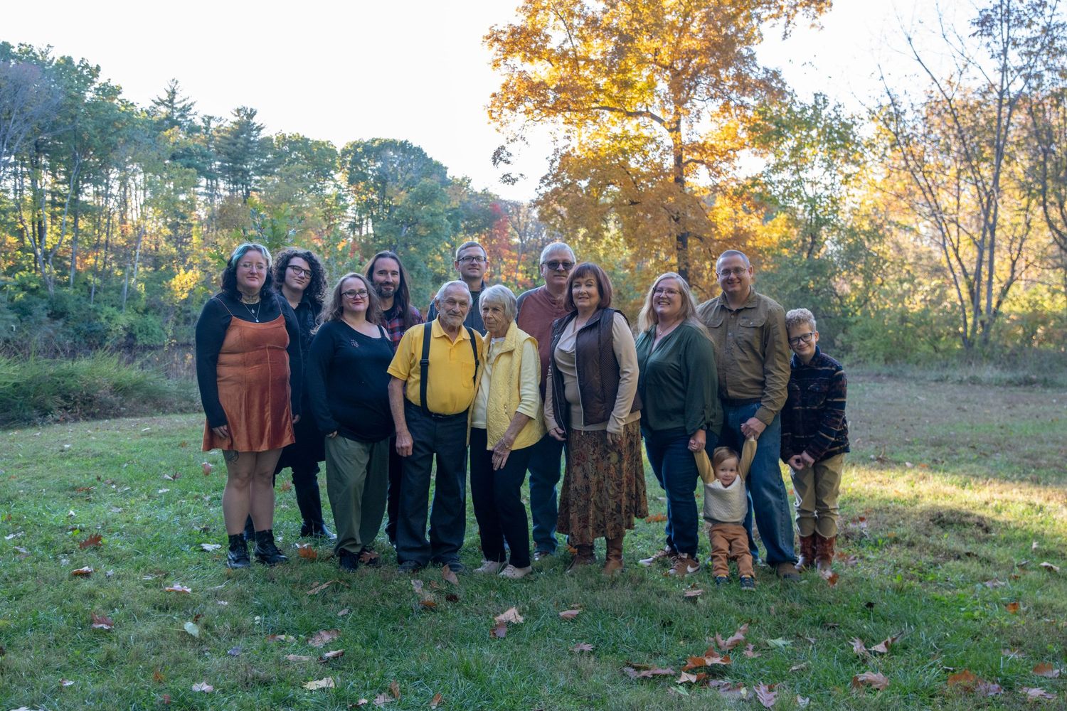 Large family group poses together outdoors during autumn with golden trees in background.